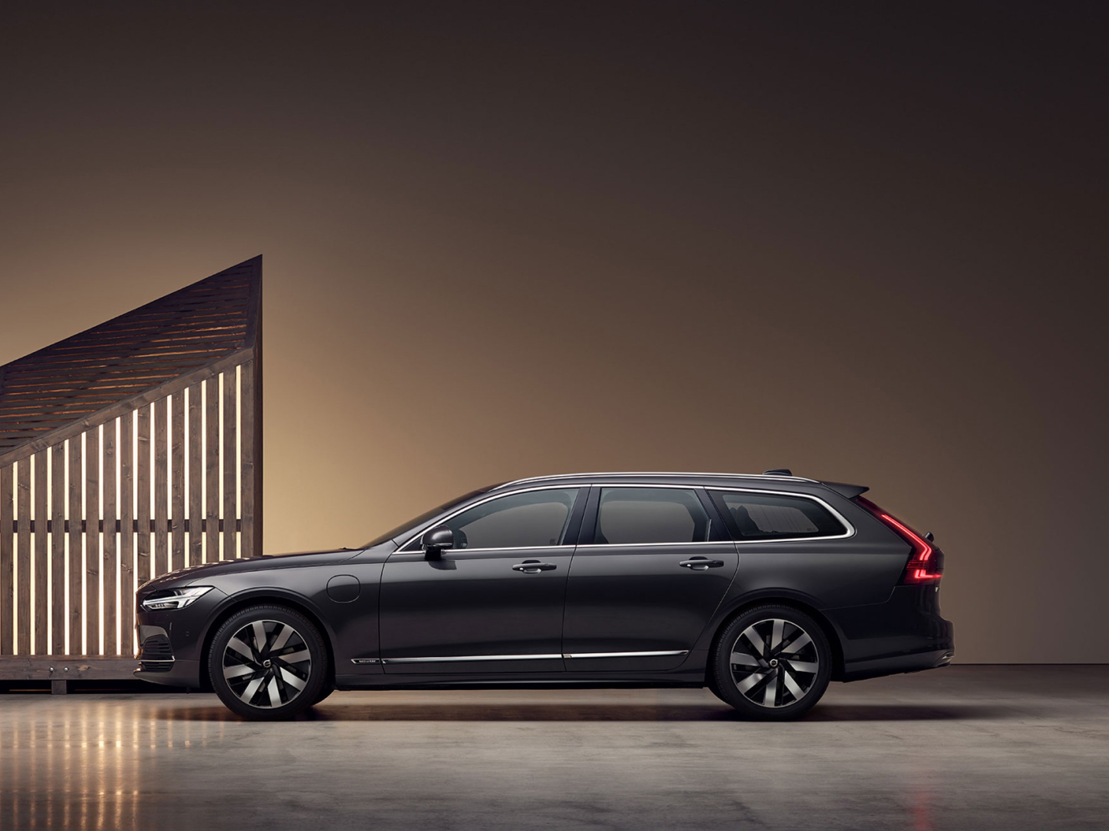 Un uomo con una giacca marrone in piedi accanto a una Volvo V90 Recharge.