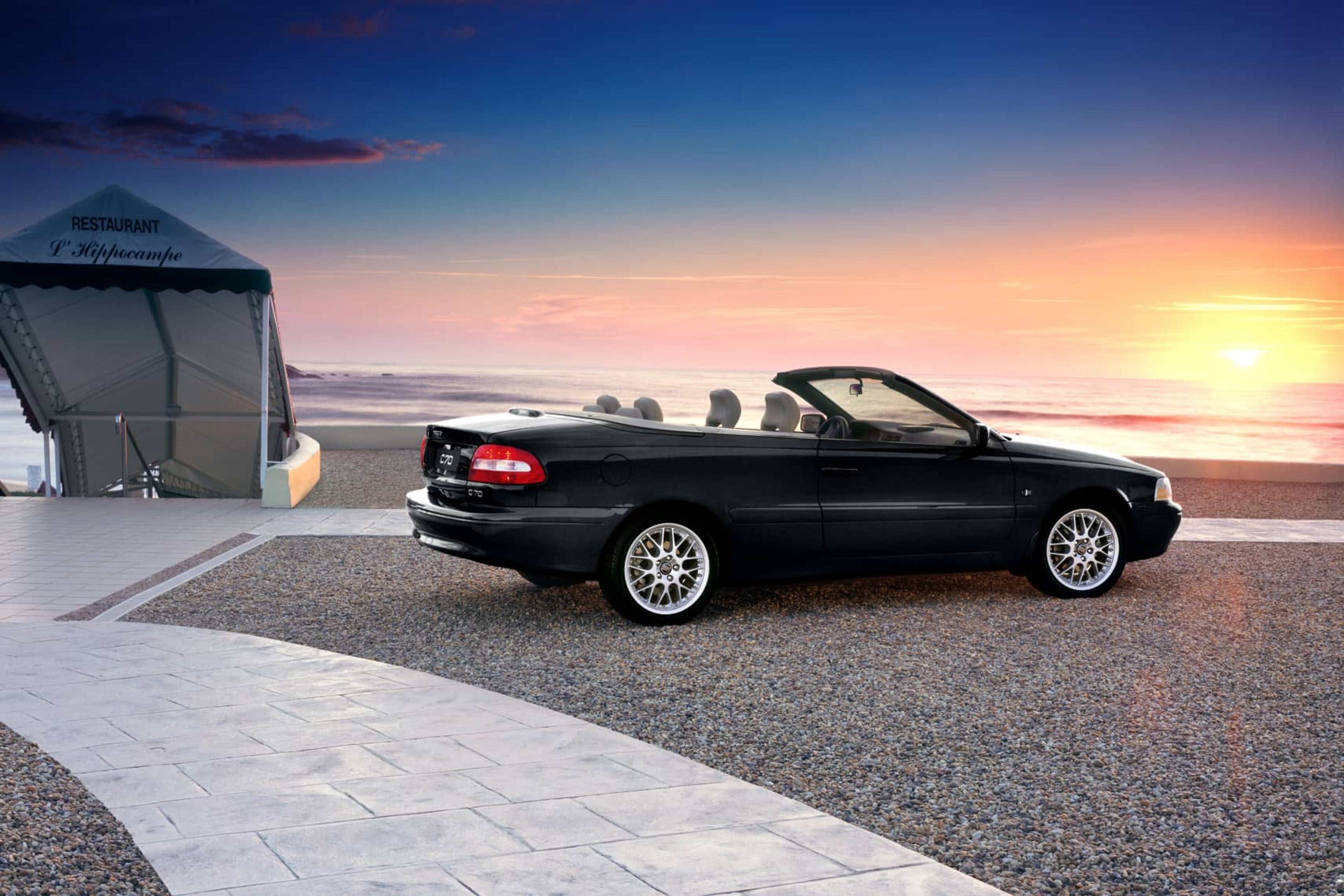 Un Volvo C70 convertible aparcado con vistas a una puesta de sol y a la playa.