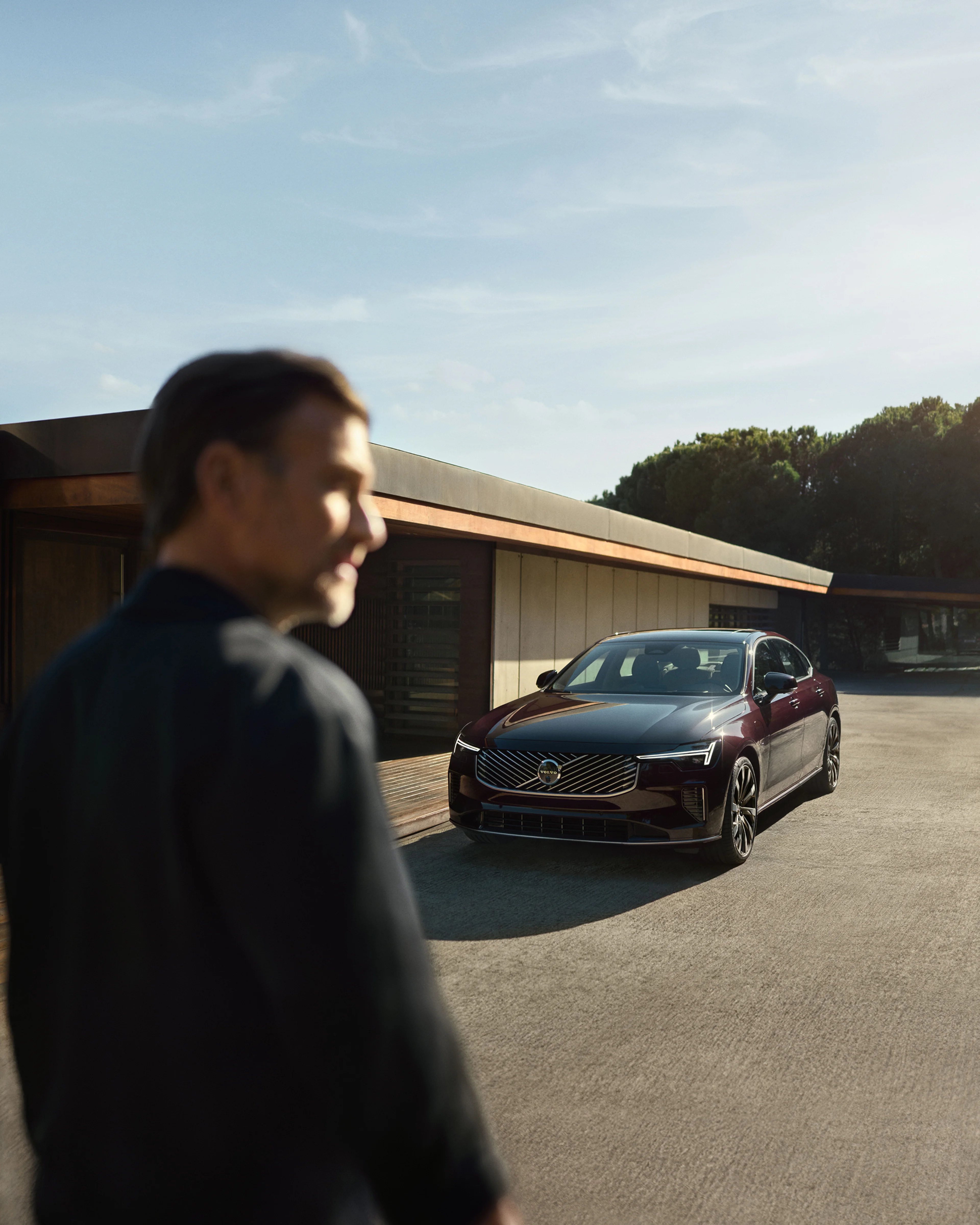 A man in the foreground with the Volvo S90 parked in front of him
