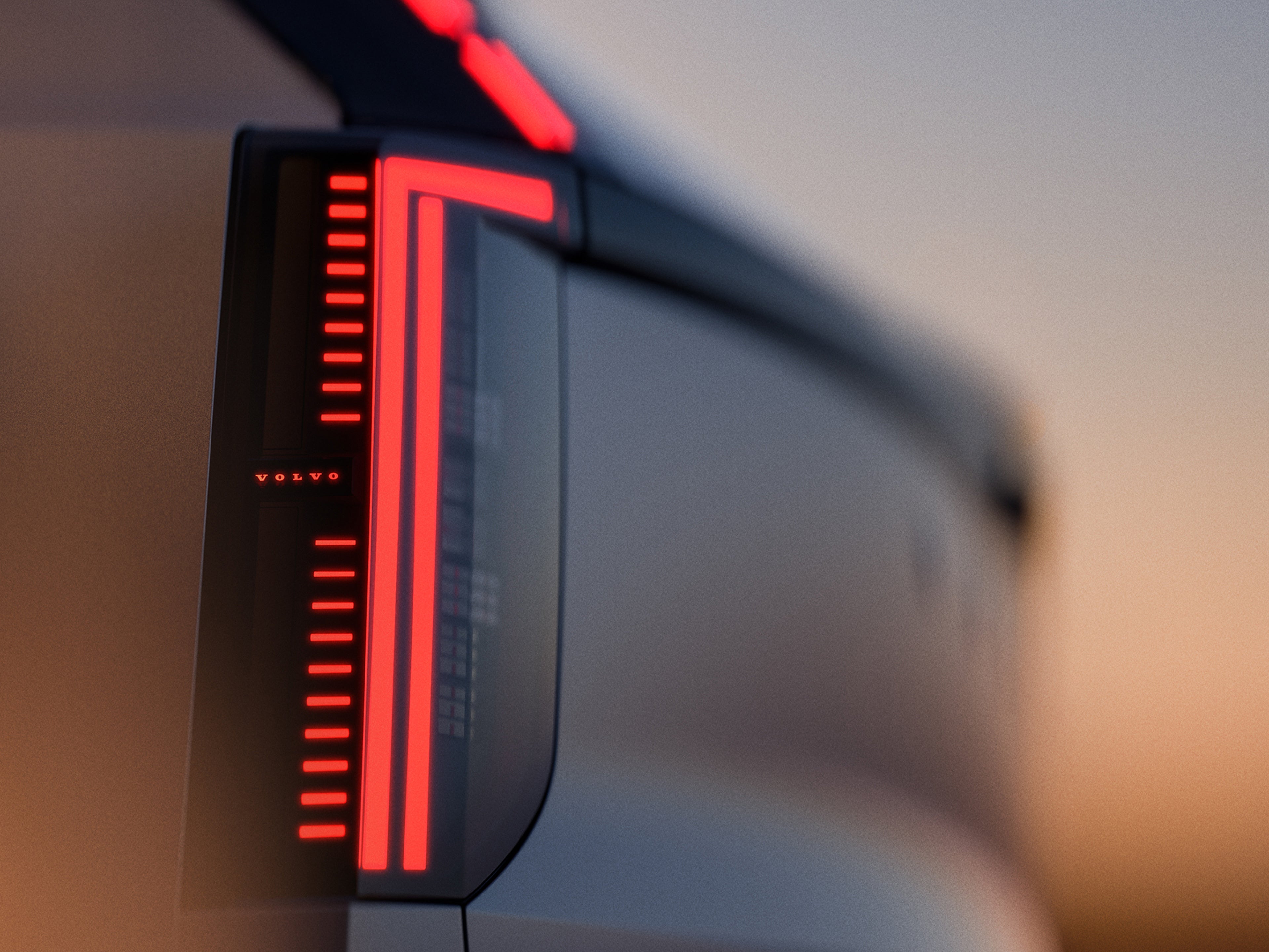 Pohled na levý zadní roh plně elektrického Volva EX60. Jeho zadní světla září červenými a oranžovými odstíny, zatímco ze zbytku prémiového SUV střední velikosti je částečně vidět silueta v nápaditém oranžově laděném prostředí.