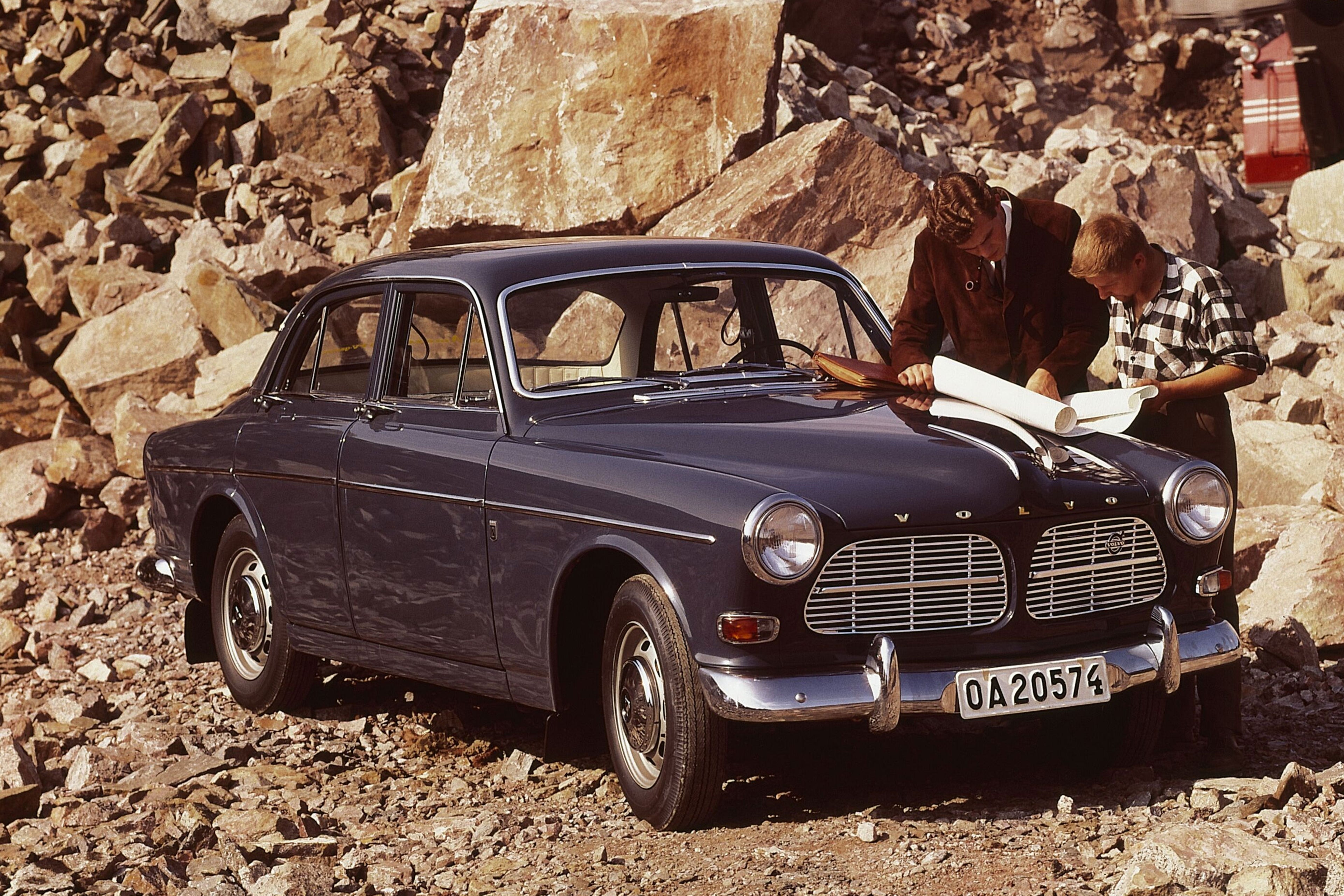 Un Volvo P1200 Amazon azul oscuro aparcado en un entorno rocoso.