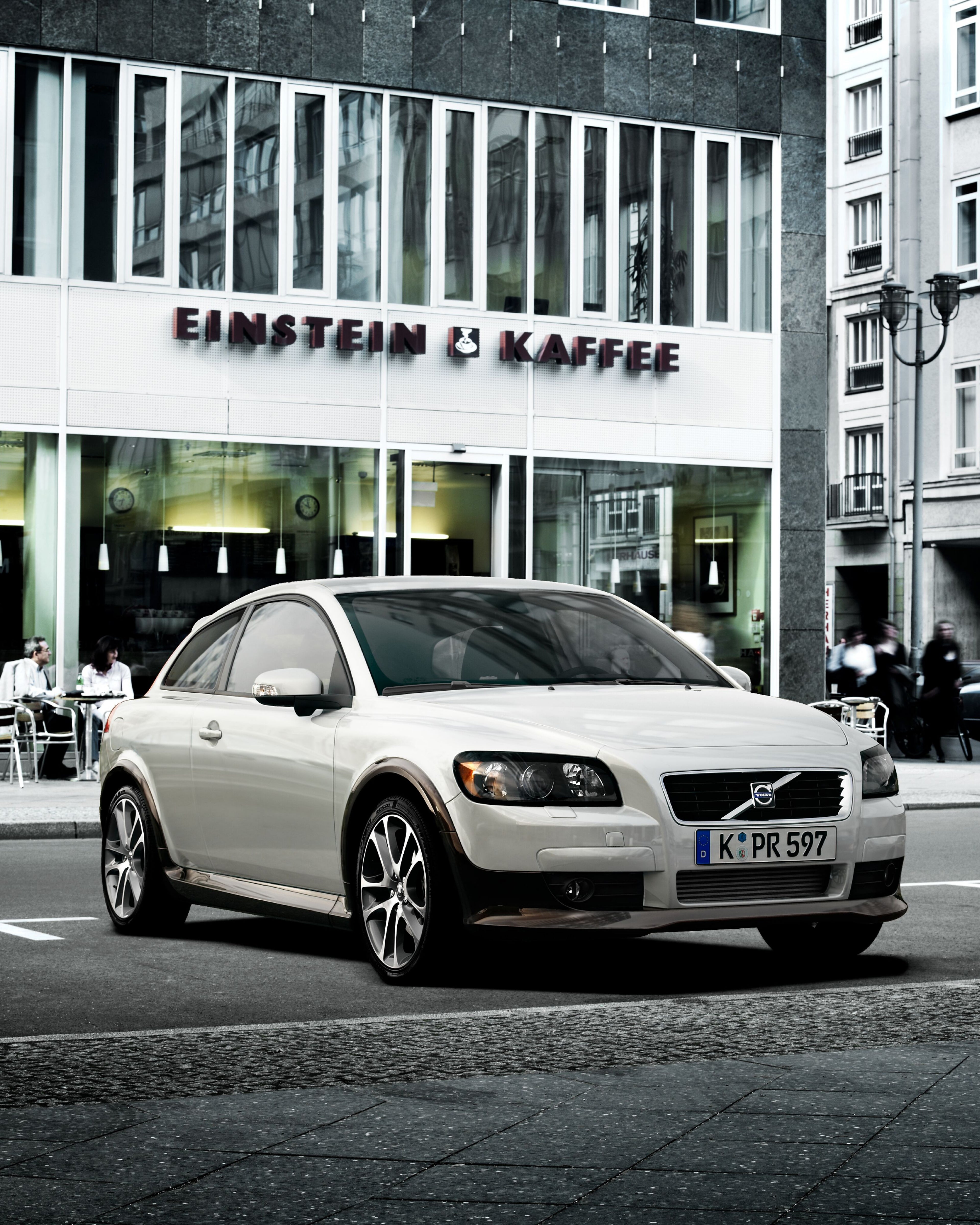 Un Volvo C30 estacionado frente a un edificio moderno.