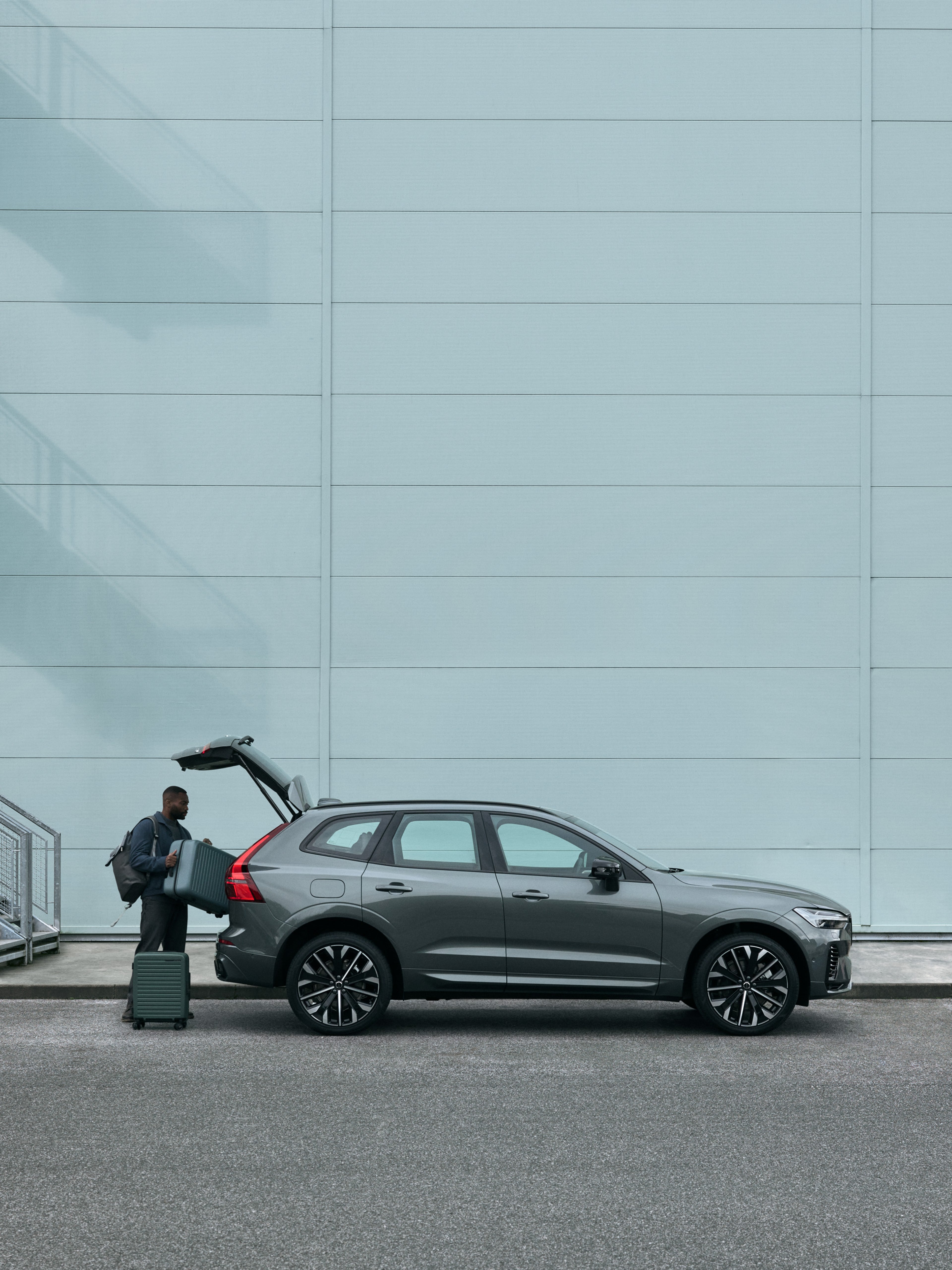Man lastar in väska i bagaget på en Volvo XC60 som står parkerad framför en industribyggnad