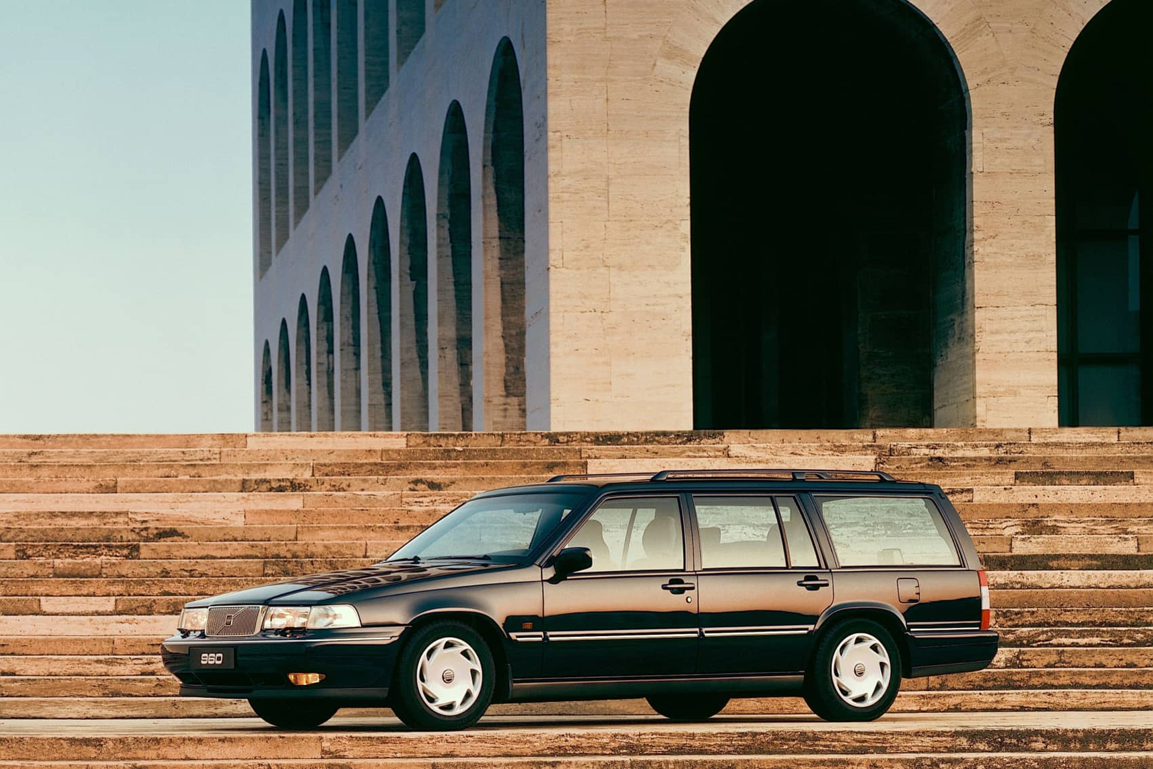 Un Volvo 960 Estate negro aparcado entre dos escaleras.