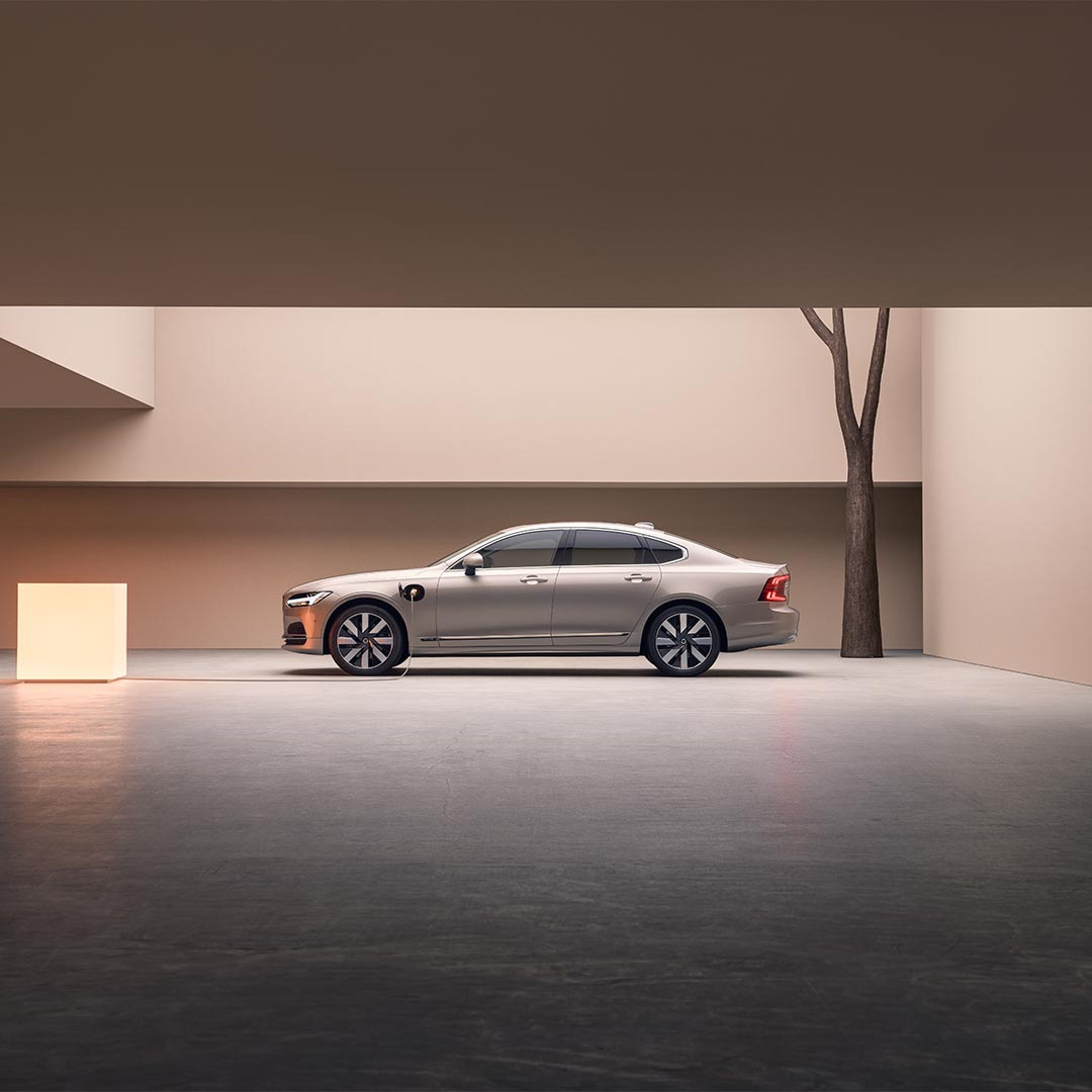 Groothoekbeeld van de linkerzijde van een Volvo S90 plug-inhybride die in een grote betonnen constructie is geparkeerd.