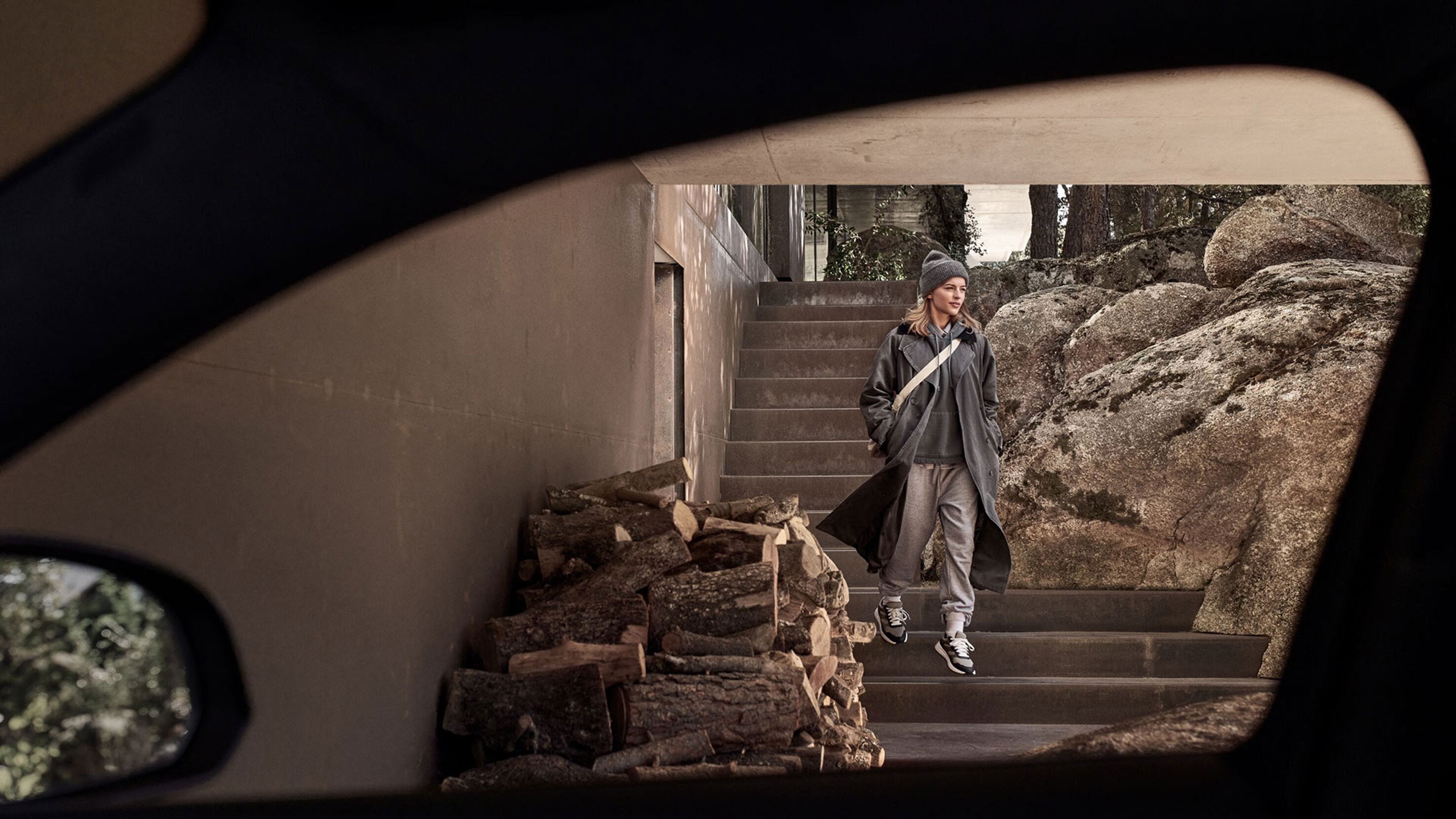 Vrouw in winterkleding die een betonnen trap afdaalt, gezien vanuit het interieur van een Volvo.