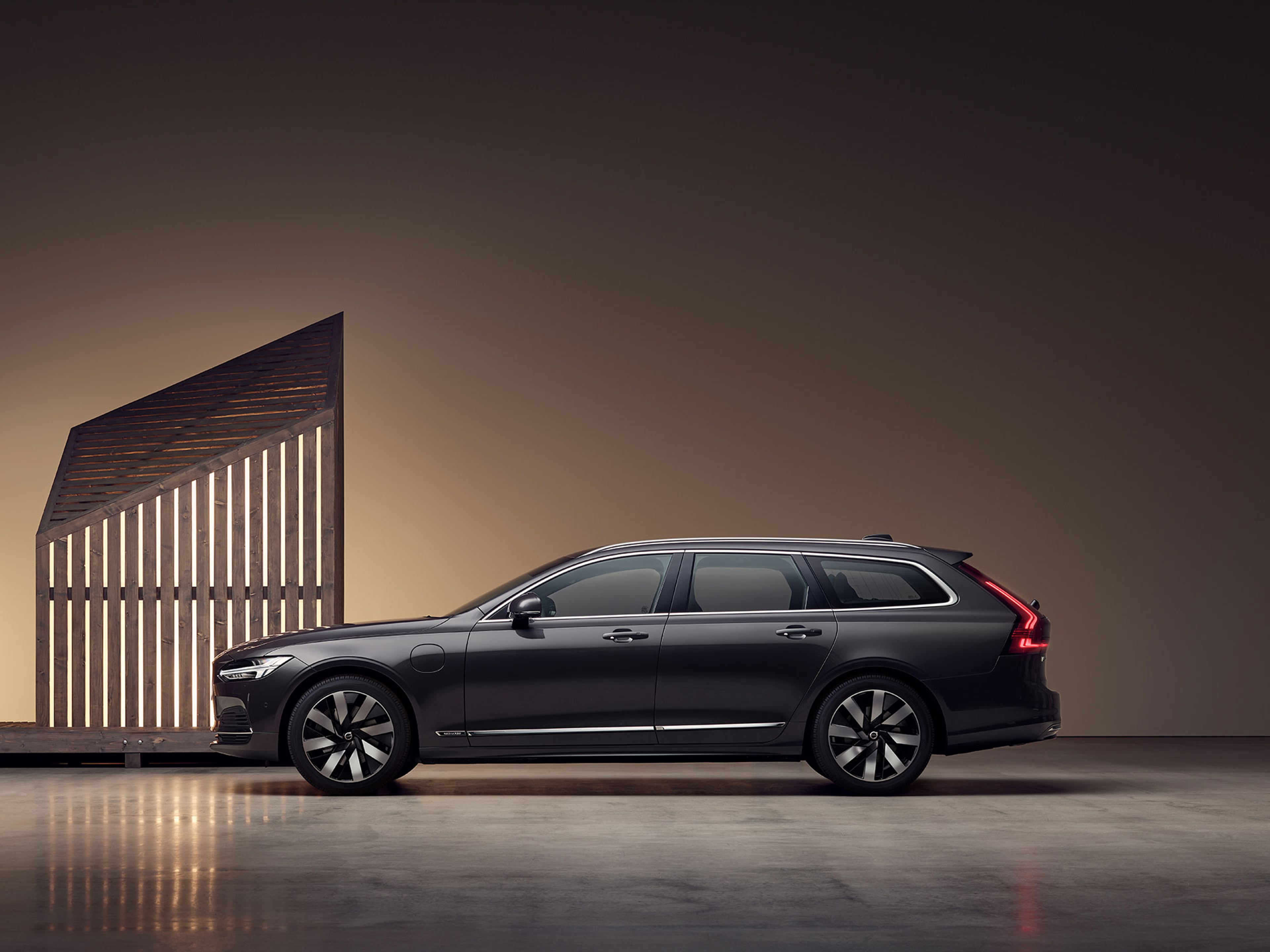 Mies ruskeassa takissa seisoo Volvo V90 Rechargen vieressä.