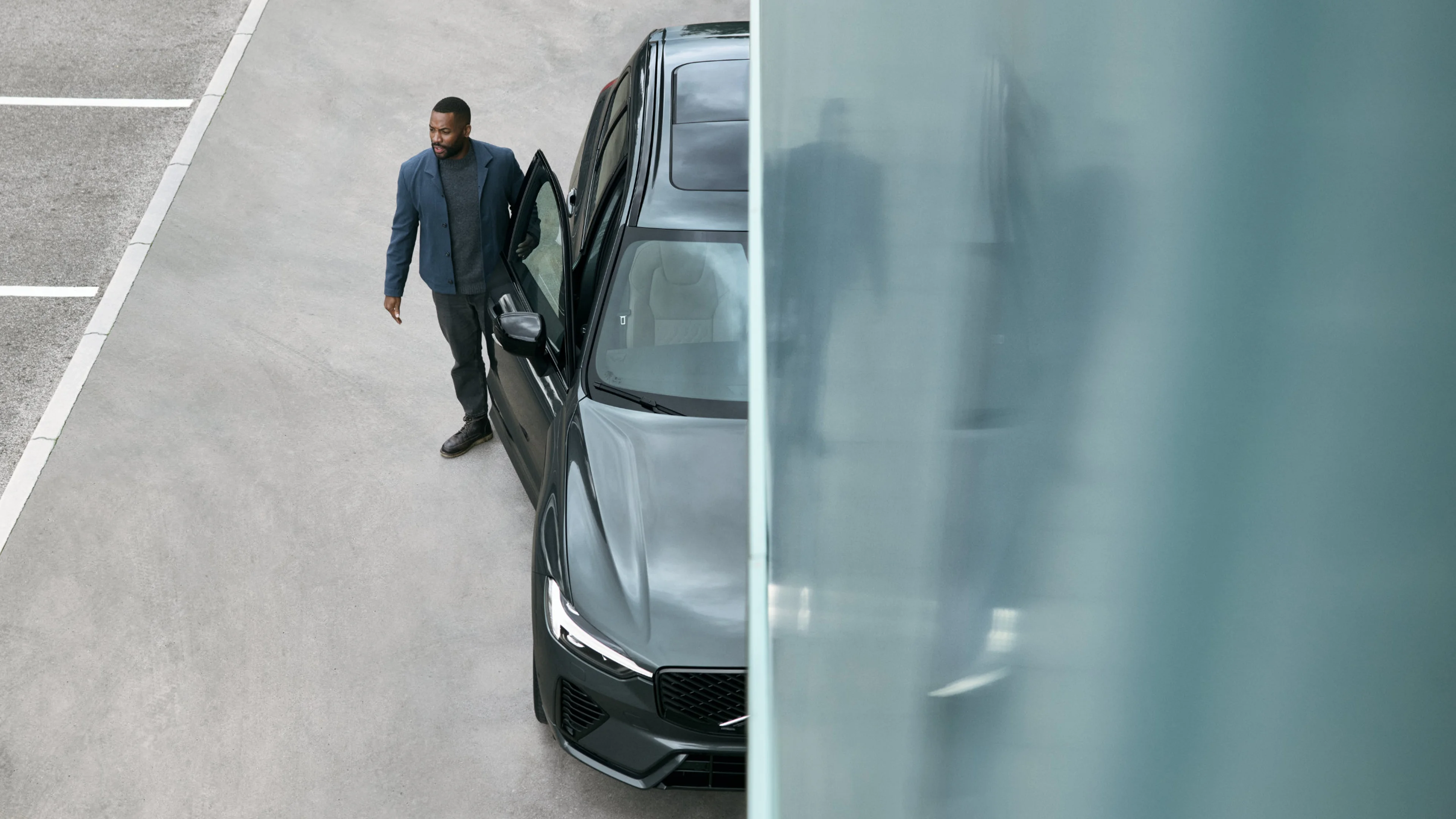 Ein mann steigt aus einem waldgrünen Volvo XC60, das Bild ist geteilt und auf der linken Seite sieht man eine leichte Spiegelung des Mannes in der grünen Fahrzeugfarbe.