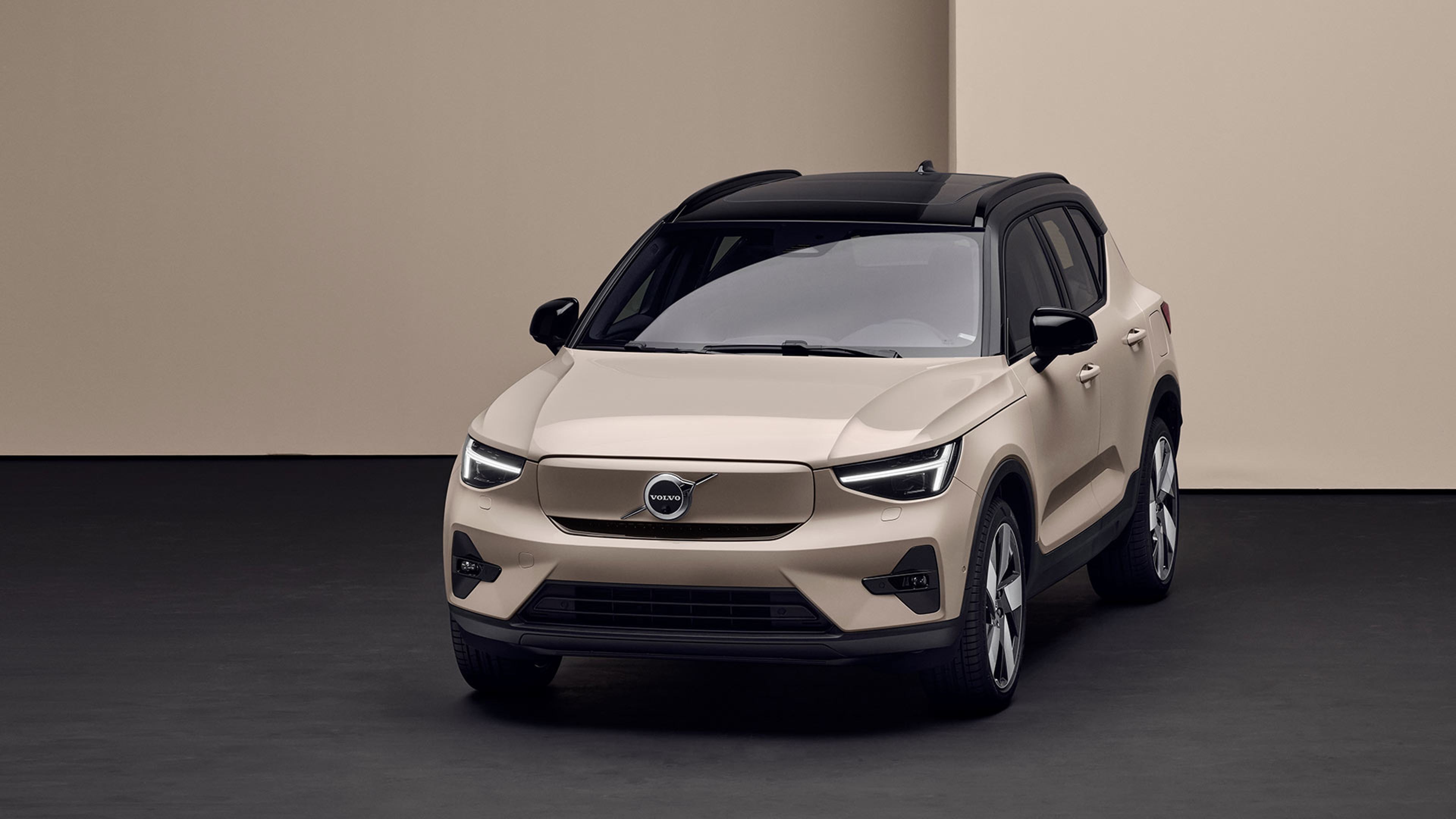 Vooraanzicht van een bronskleurige Volvo EX40 met een zwart dak, geparkeerd in een studio.