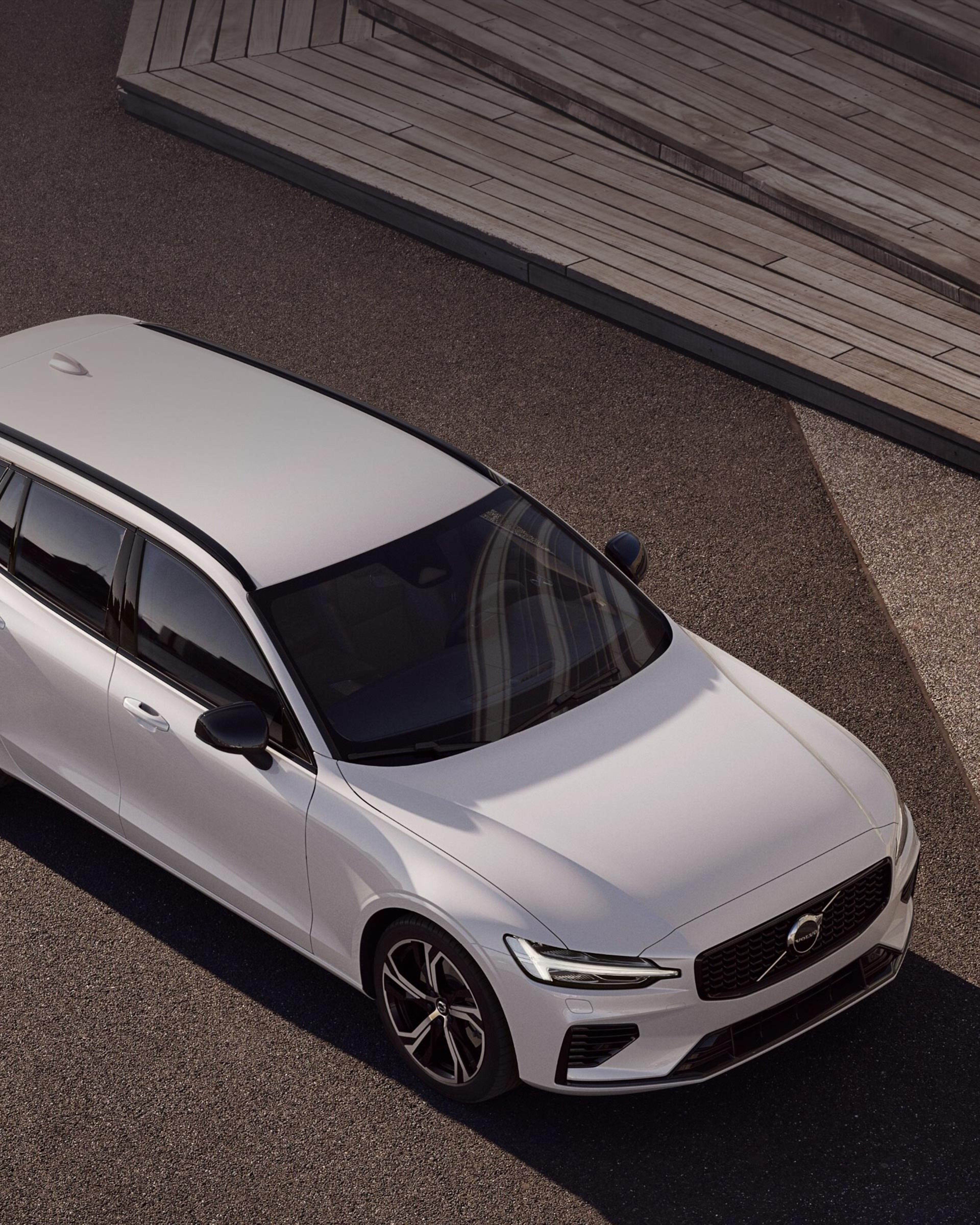 Ruskealle soralle pysäköity Crystal white värinen Volvo V60 lataushybridifarmariauto yläviistosta kuvattuna.