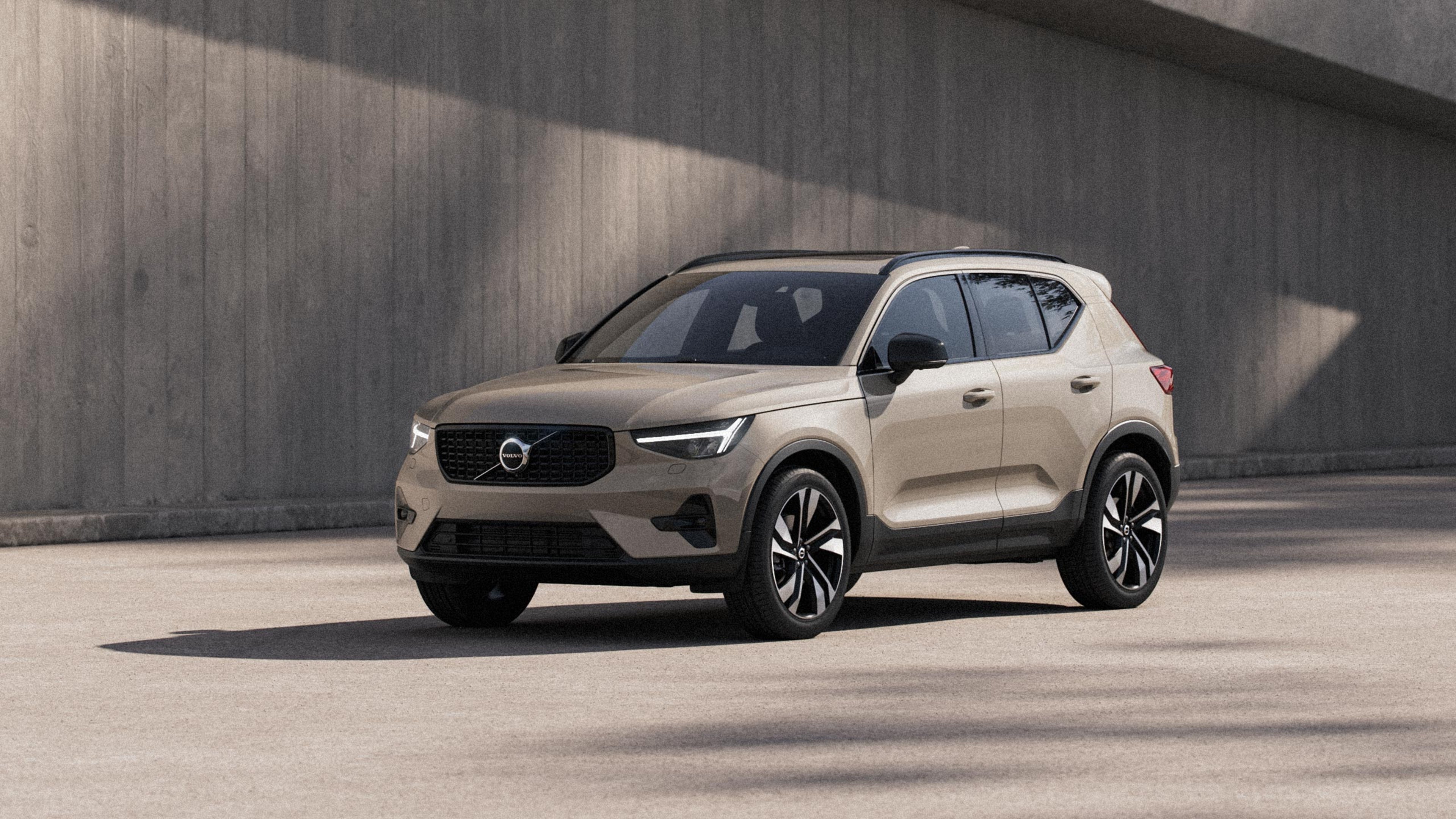 Sand dune -värinen Volvo XC40 kevythybridikatumaasturi pysäköitynä betoniseinän eteen.