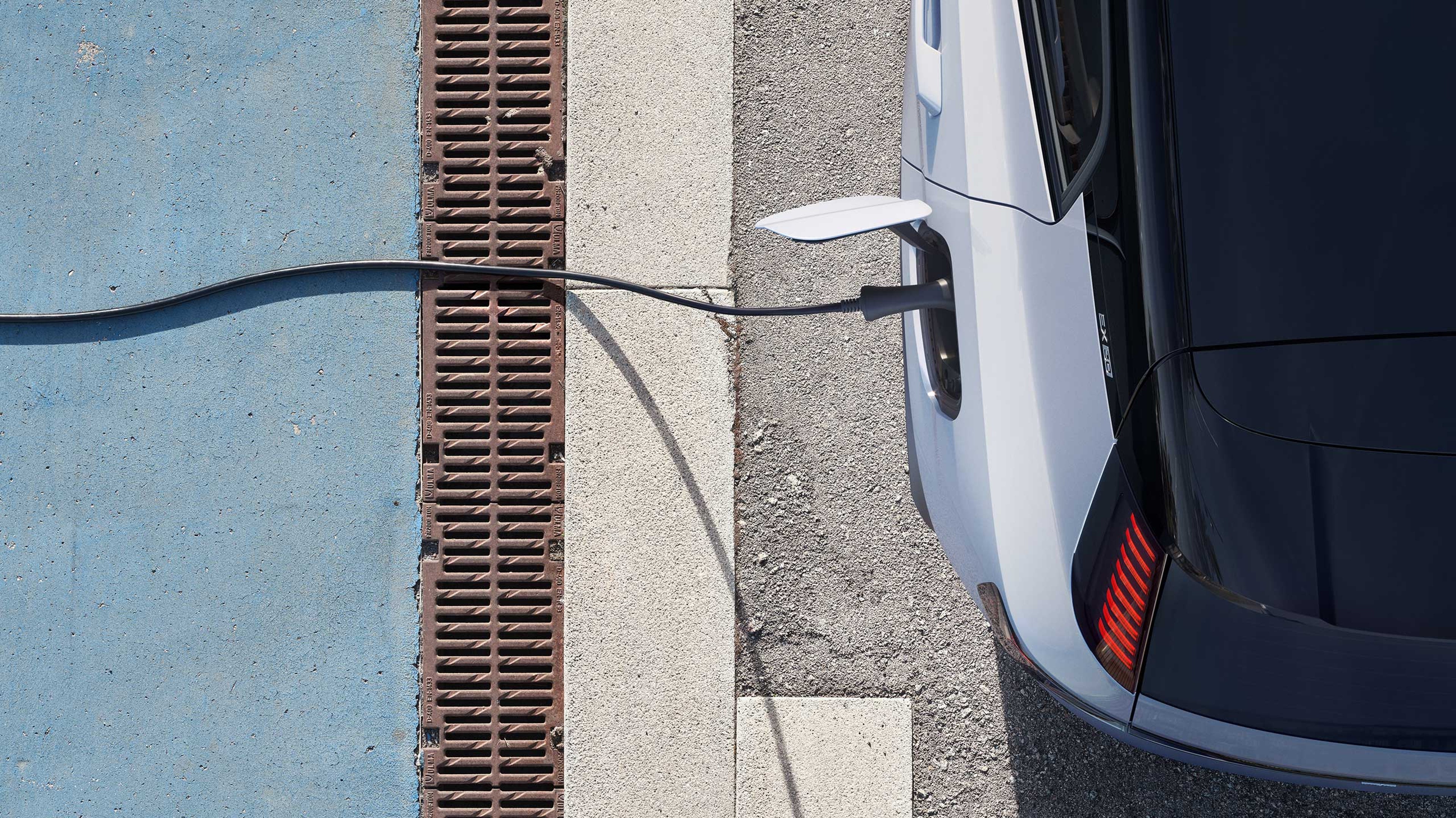 Lataukseen kytketyn Cloud blue -värisen Volvo EX30 täyssähköisen katumaasturin perä ylhäältäpäin kuvattuna.