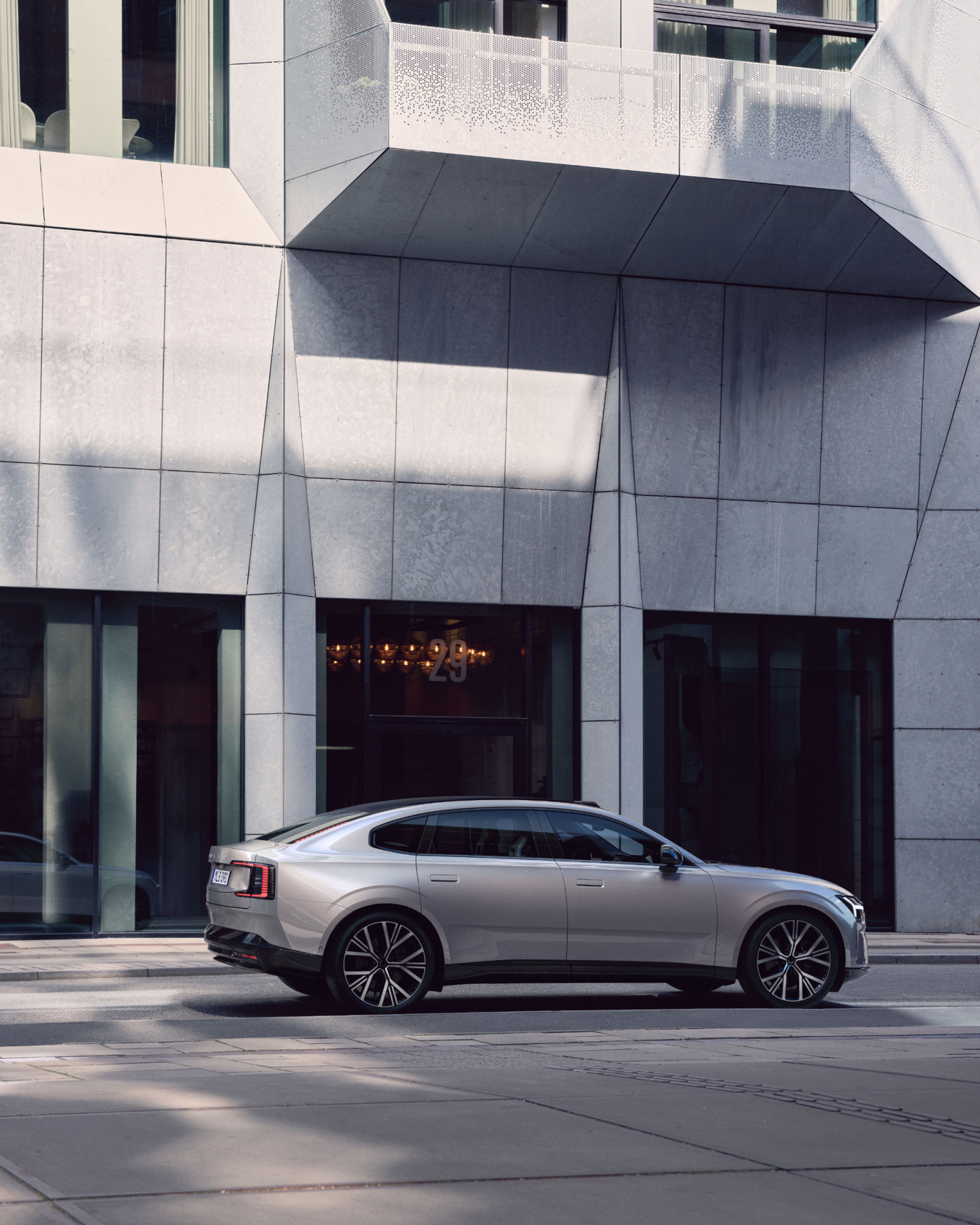 Вид сбоку на полностью электрический Volvo ES90 перед современным зданием.