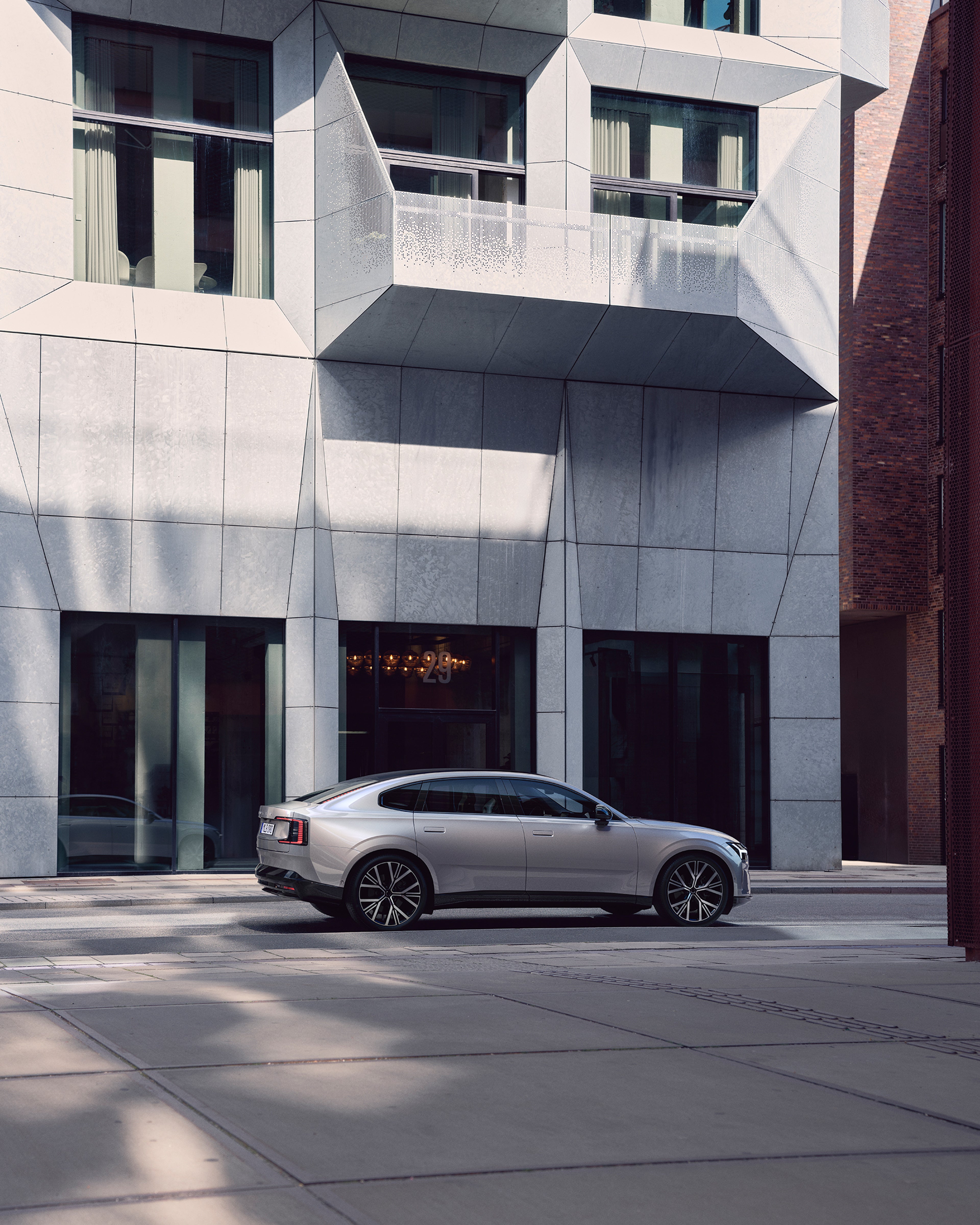 Pilnībā elektriskās Volvo ES90 sānskats modernas ēkas priekšā.