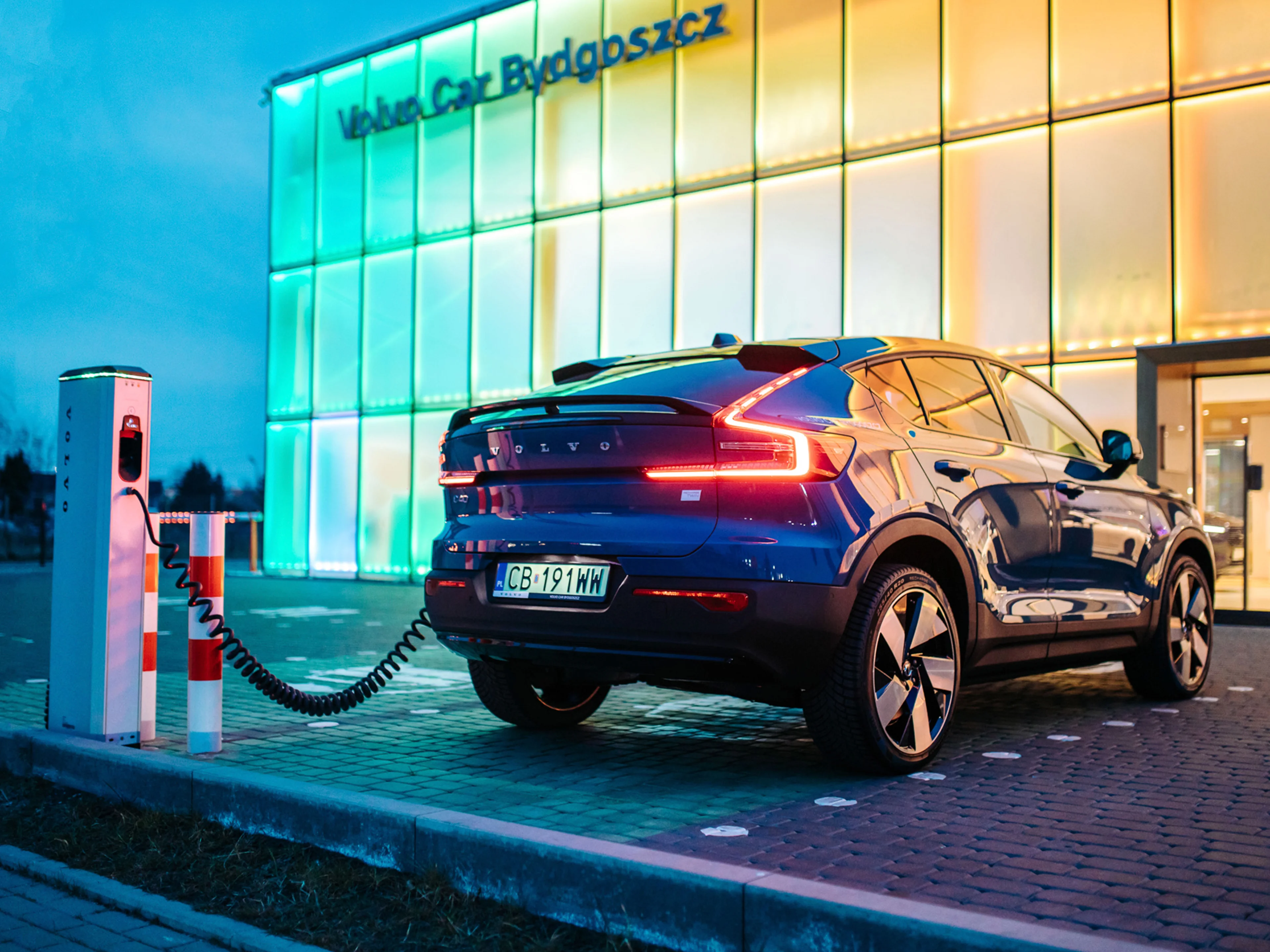 Volvo C40 stojące tyłoprzodem podłączone do ładowarki na tle podświetlonej elewacji Volvo