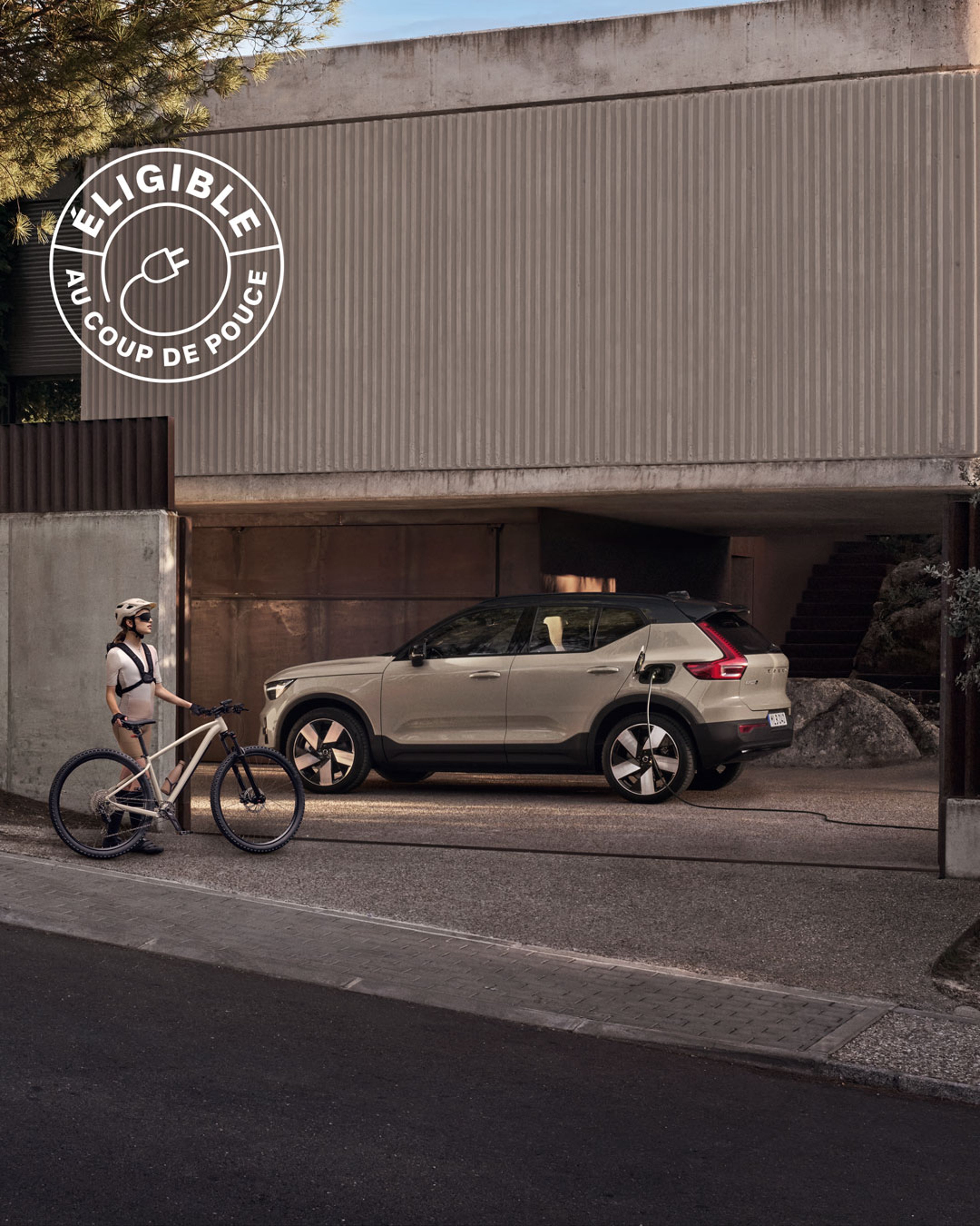 Femme avec vélo devant une Volvo EX40 électrique en charge dans une allée.