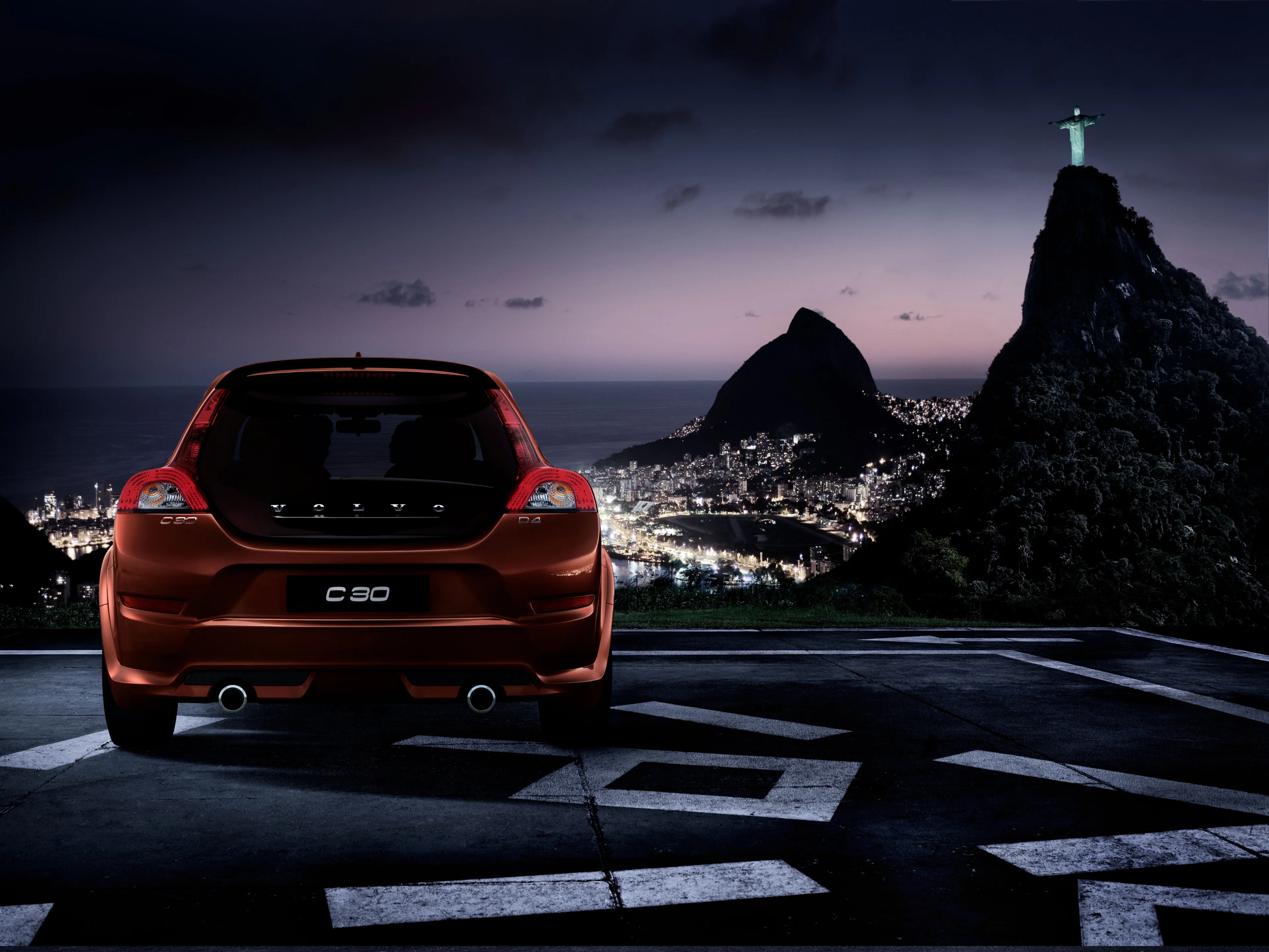 Photo d’une Volvo C30 vue de l’arrière avec vue d’une ville de nuit.