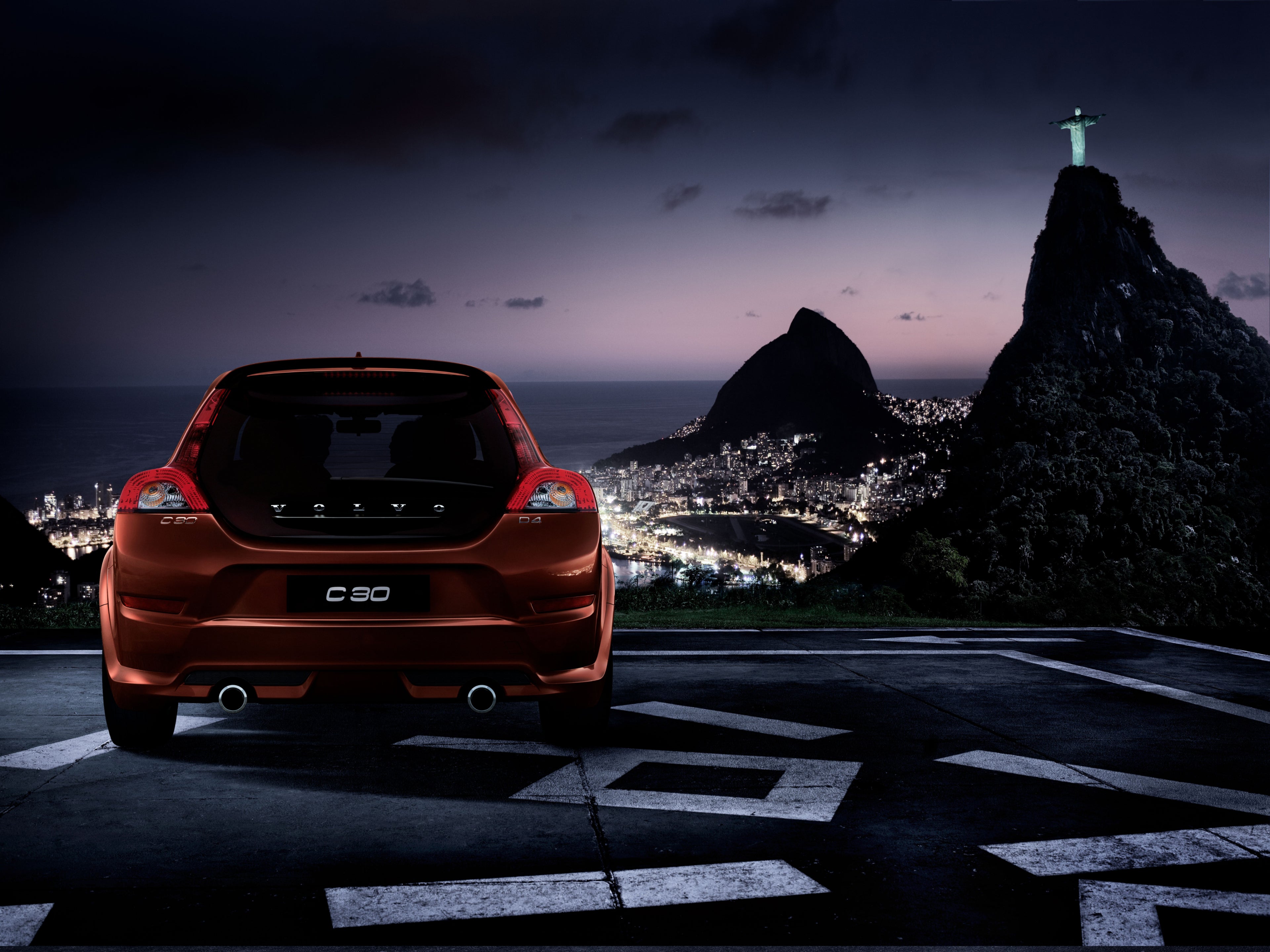 Una foto de un Volvo C30 desde atrás con vistas a una ciudad de noche.