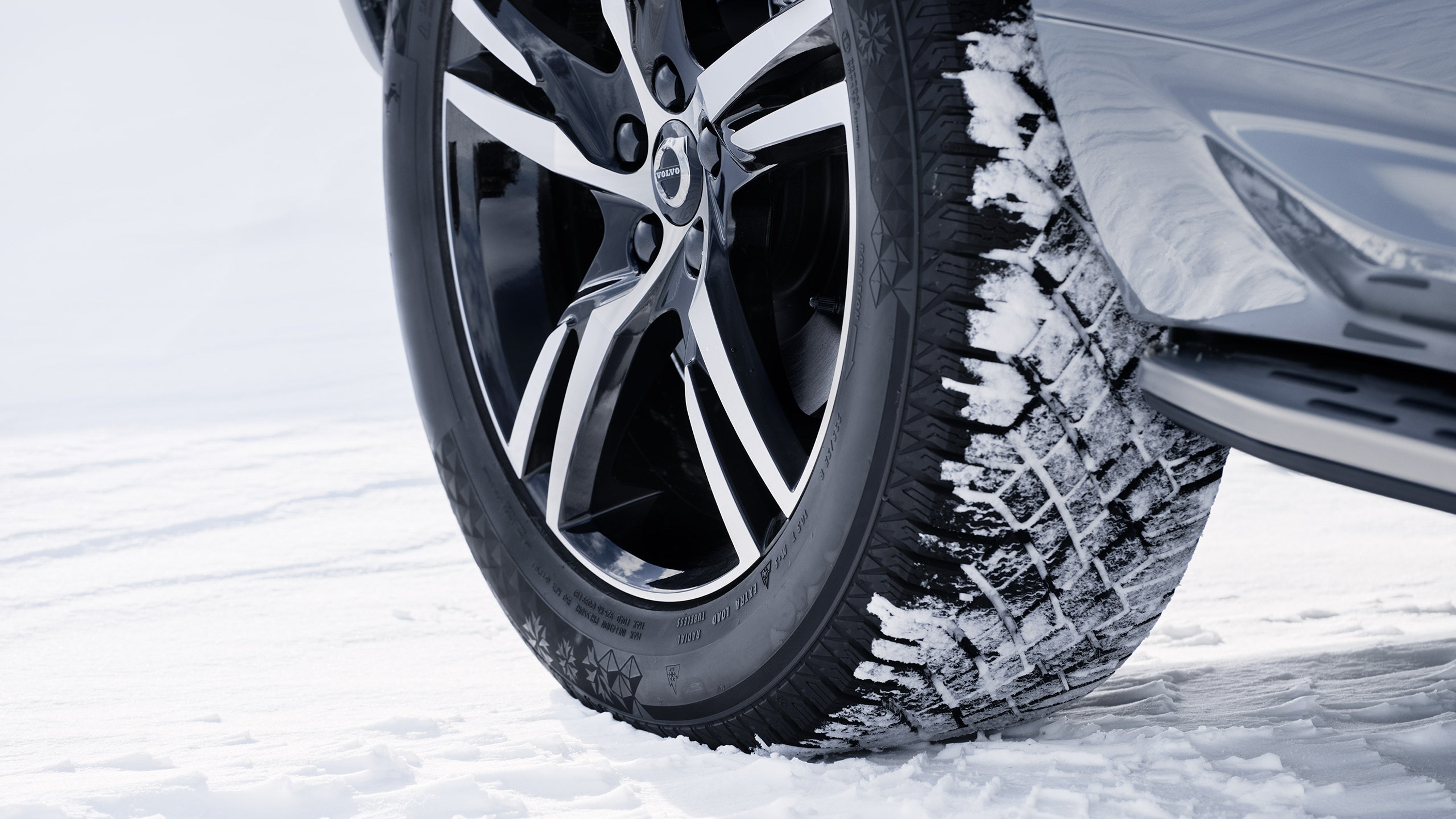 Lähikuva Volvo lataushybridiauton oikeasta takapyörästä ja lumisesta talvirenkaasta lumista maata vasten.