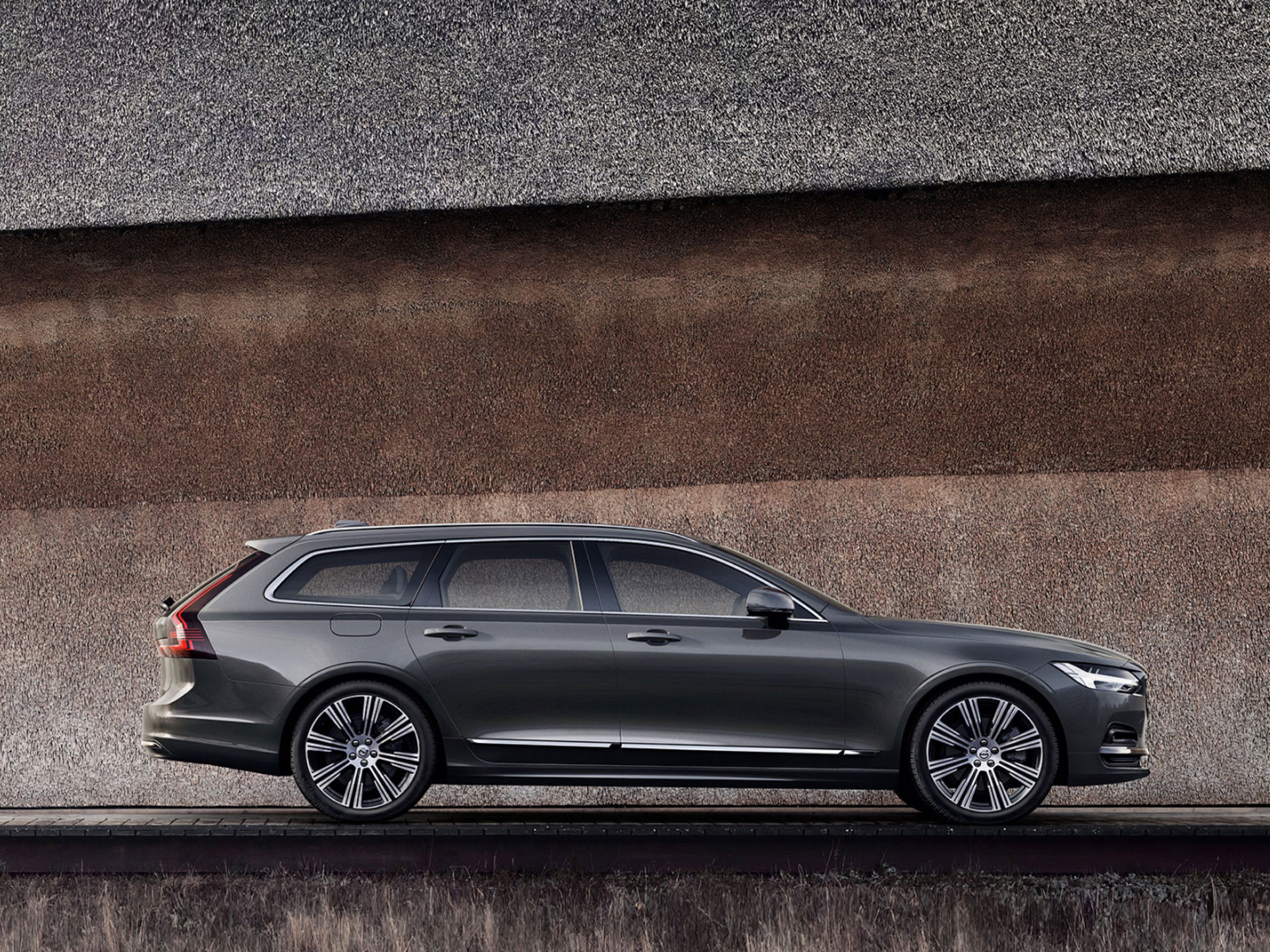 Uma Volvo V90 em cinza-escuro estaciona junto a uma parede.