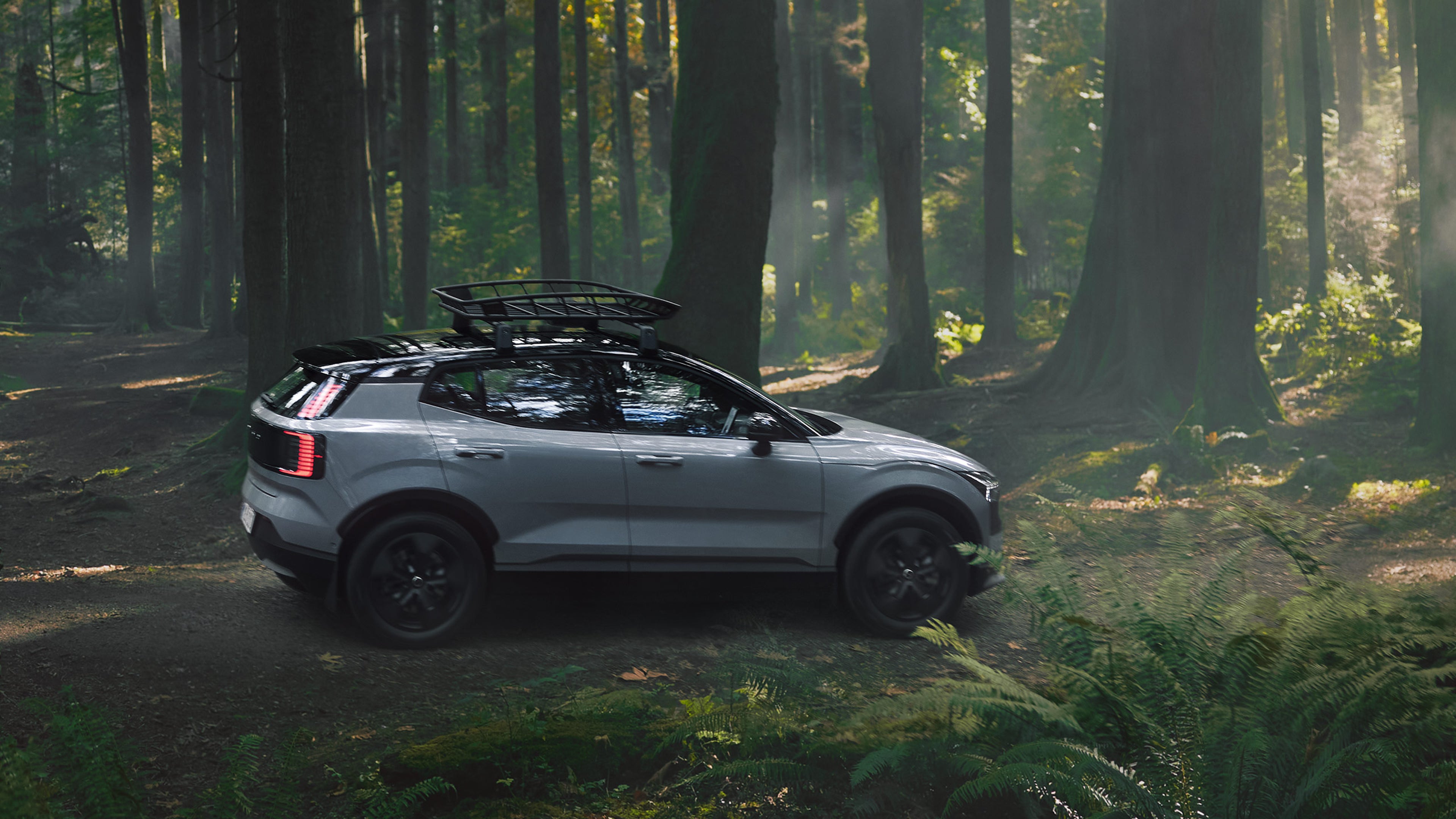 Cloud Blue -värinen Volvo EX30 Cross Country täyssähköinen katumaasturi pysäköitynä metsän keskelle. Auringon valo siivilöityy latvojen välistä.