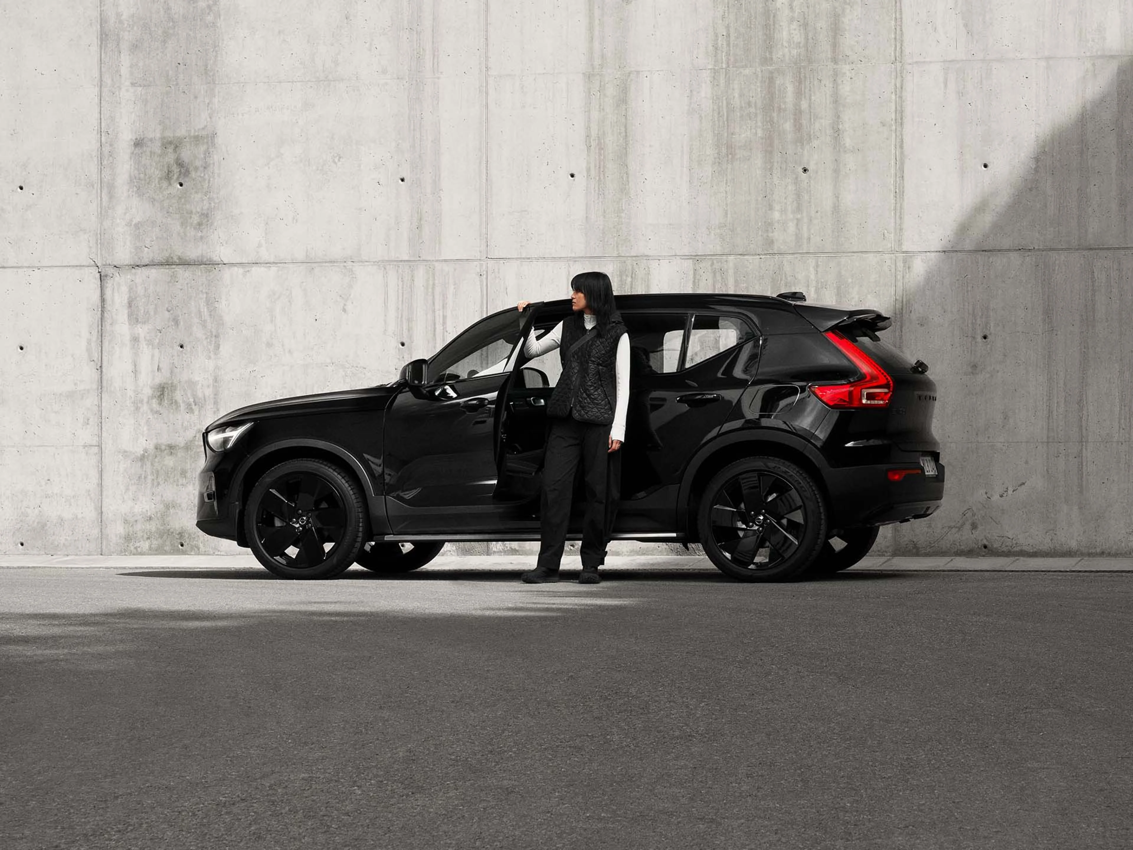 Seitenansicht des Volvo EX40 Black Edition an dem eine Frau steht.