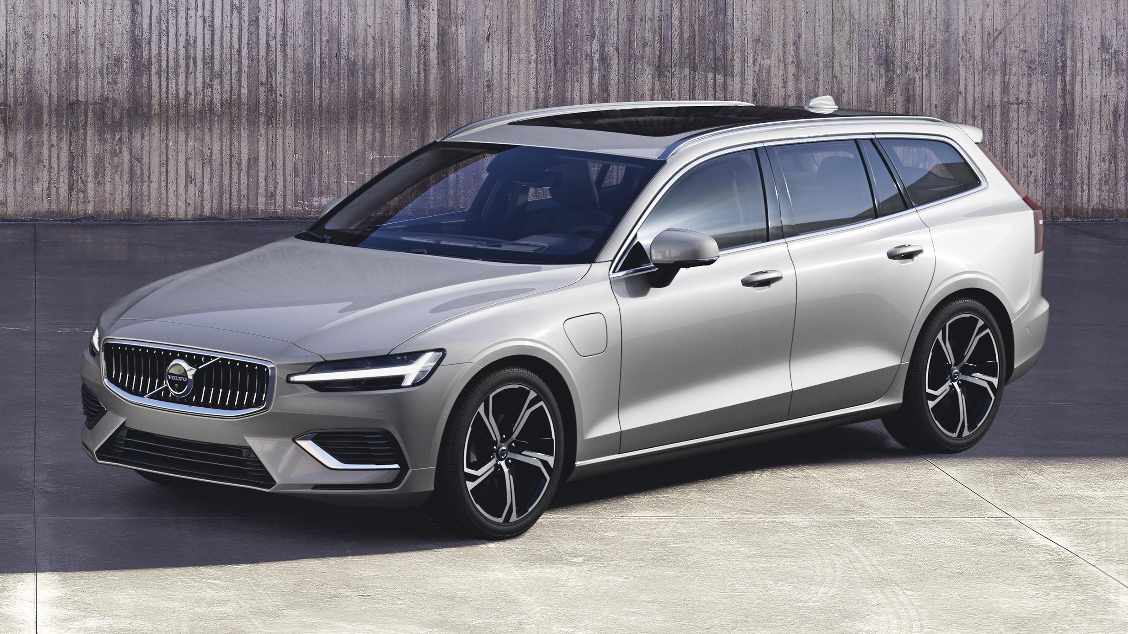 Dawn silver -värinen Volvo V60 lataushybridifarmari pysäköitynä betonialustalle. Taustalla betoniseinä, jonka pinnassa on pystysuuntaisia uurteita.
