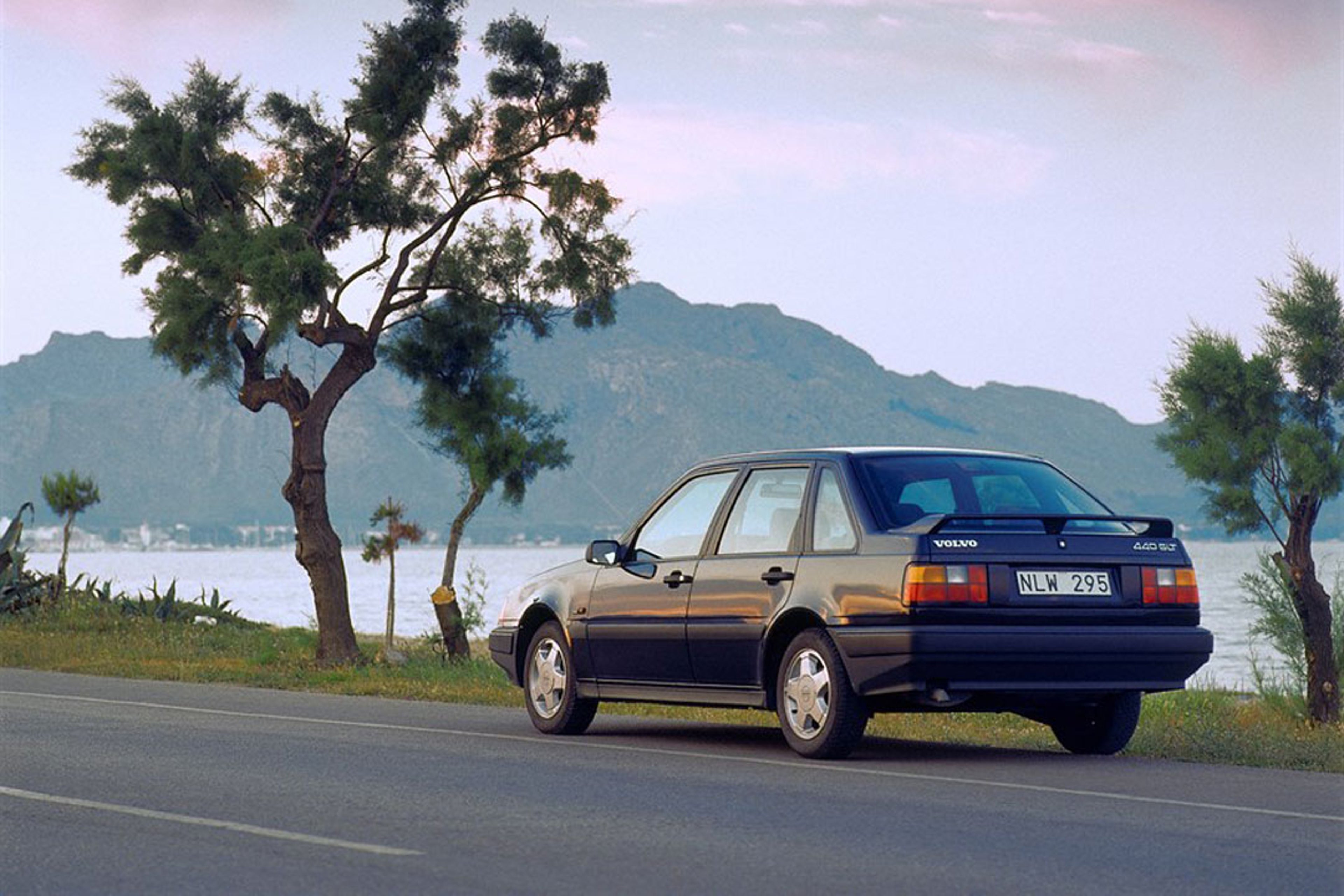 Volvo 440 garé sur la plage avec une planche de surf sur la galerie de toit.