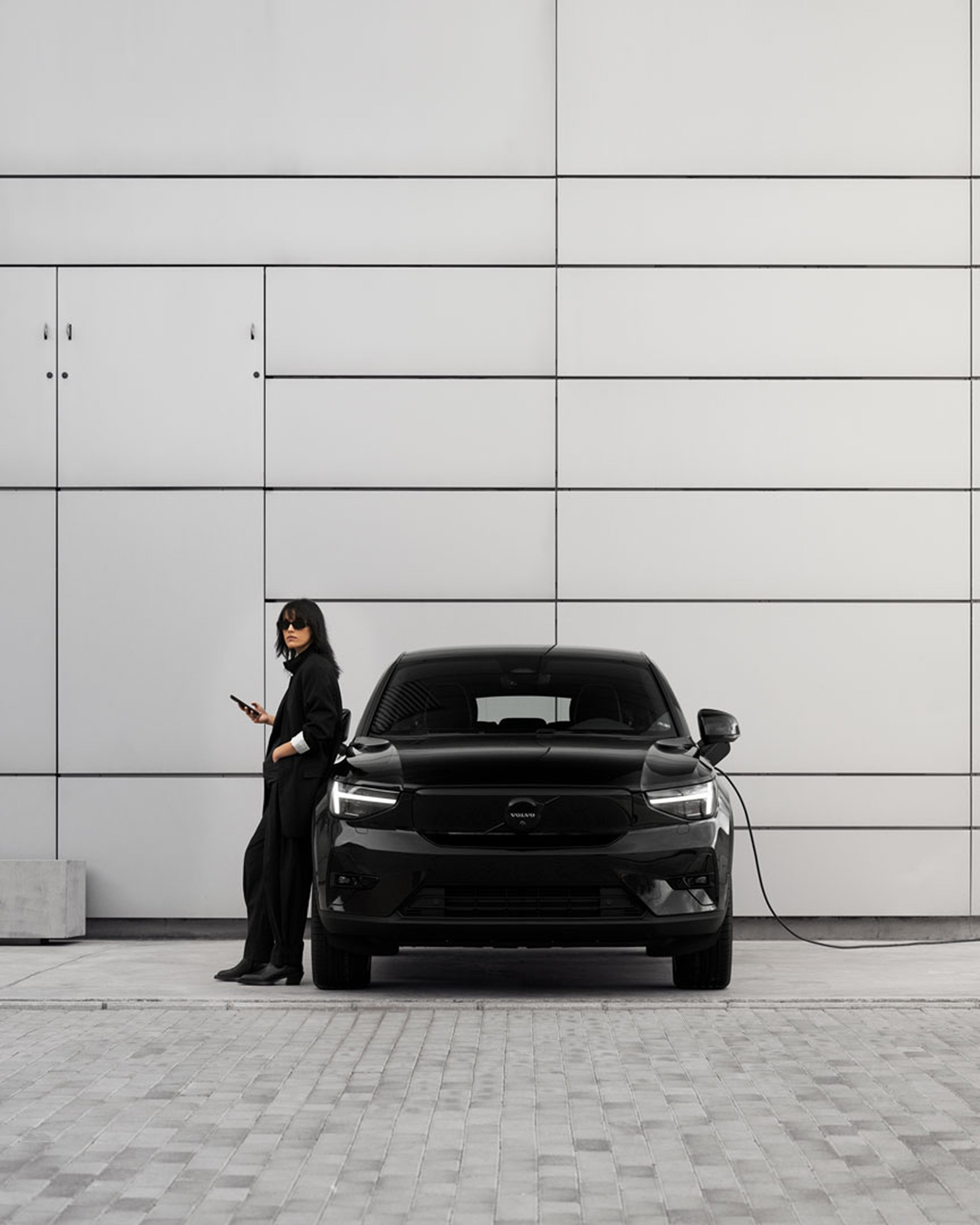 A woman stands beside a front-facing Volvo EC40 Electric, leaning casually on its side.
