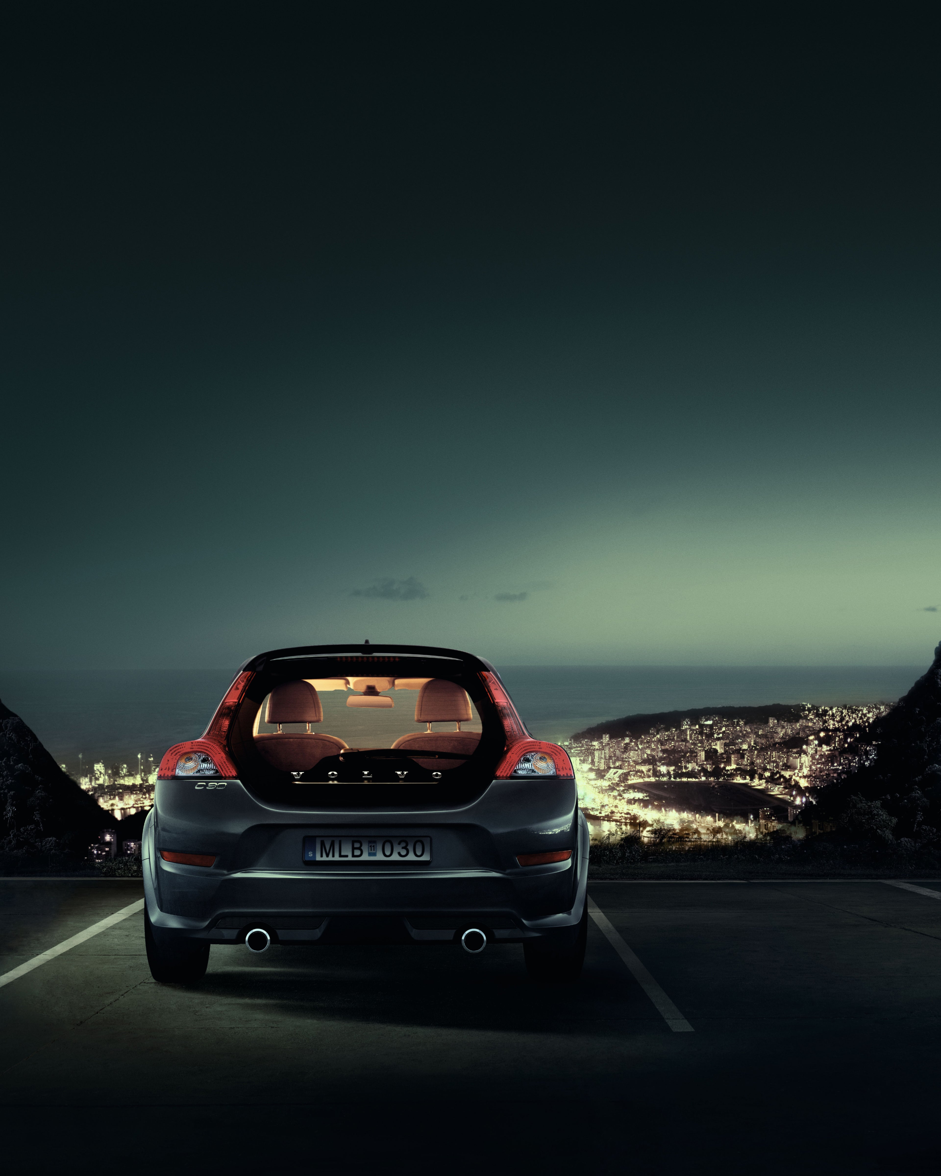 Imagem noturna de um Volvo C30 estacionado com vista sobre uma cidade.