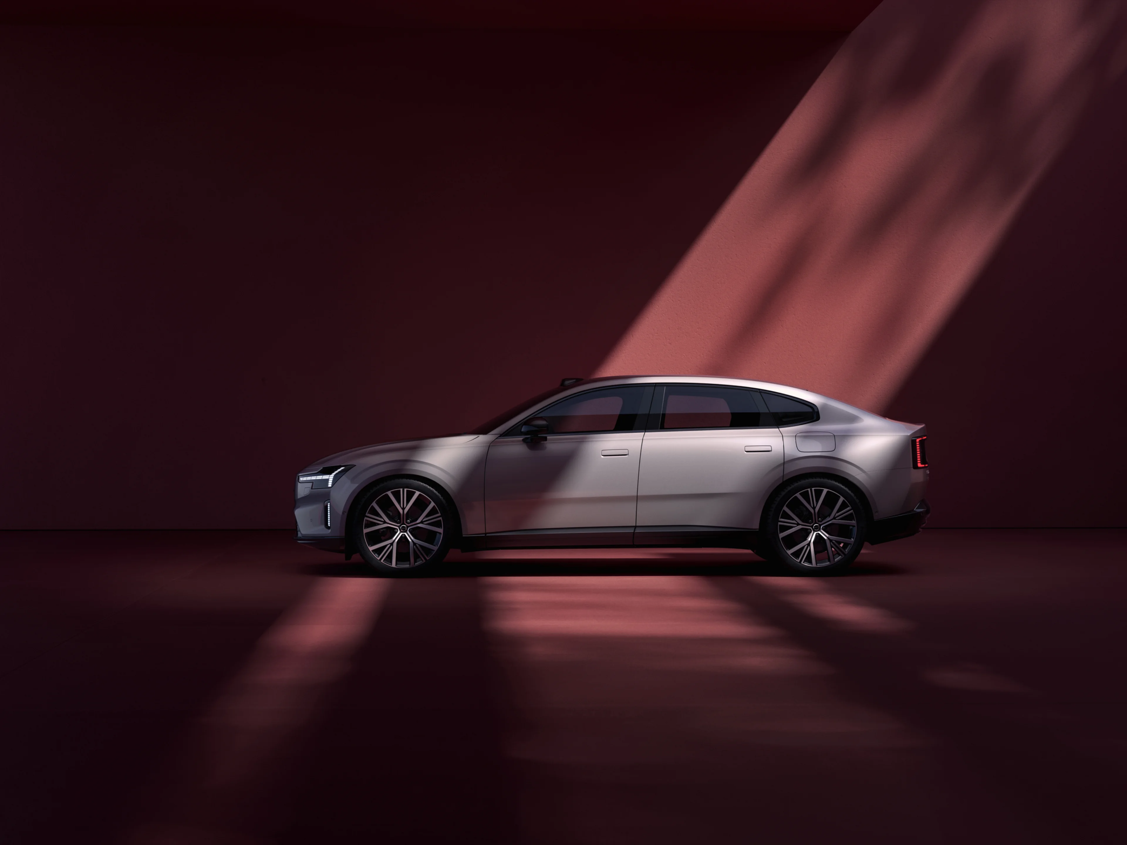 Digital artwork front shot of a Volvo ES90 positioned on a seesaw against a deep red background. Only the windscreen, roof and side mirrors are visible.