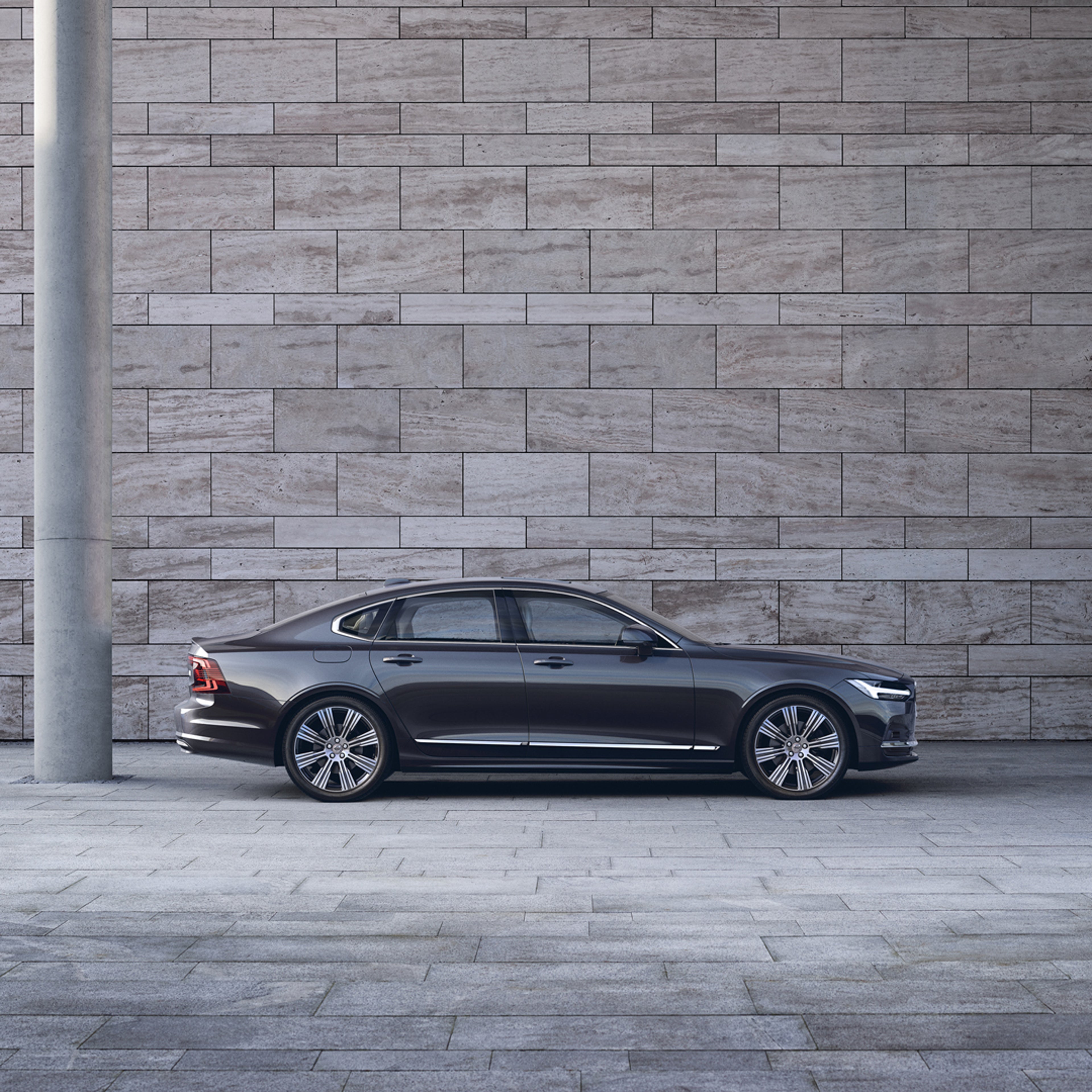 Volvo S90 seen from side parked in front of grey concrete wall.