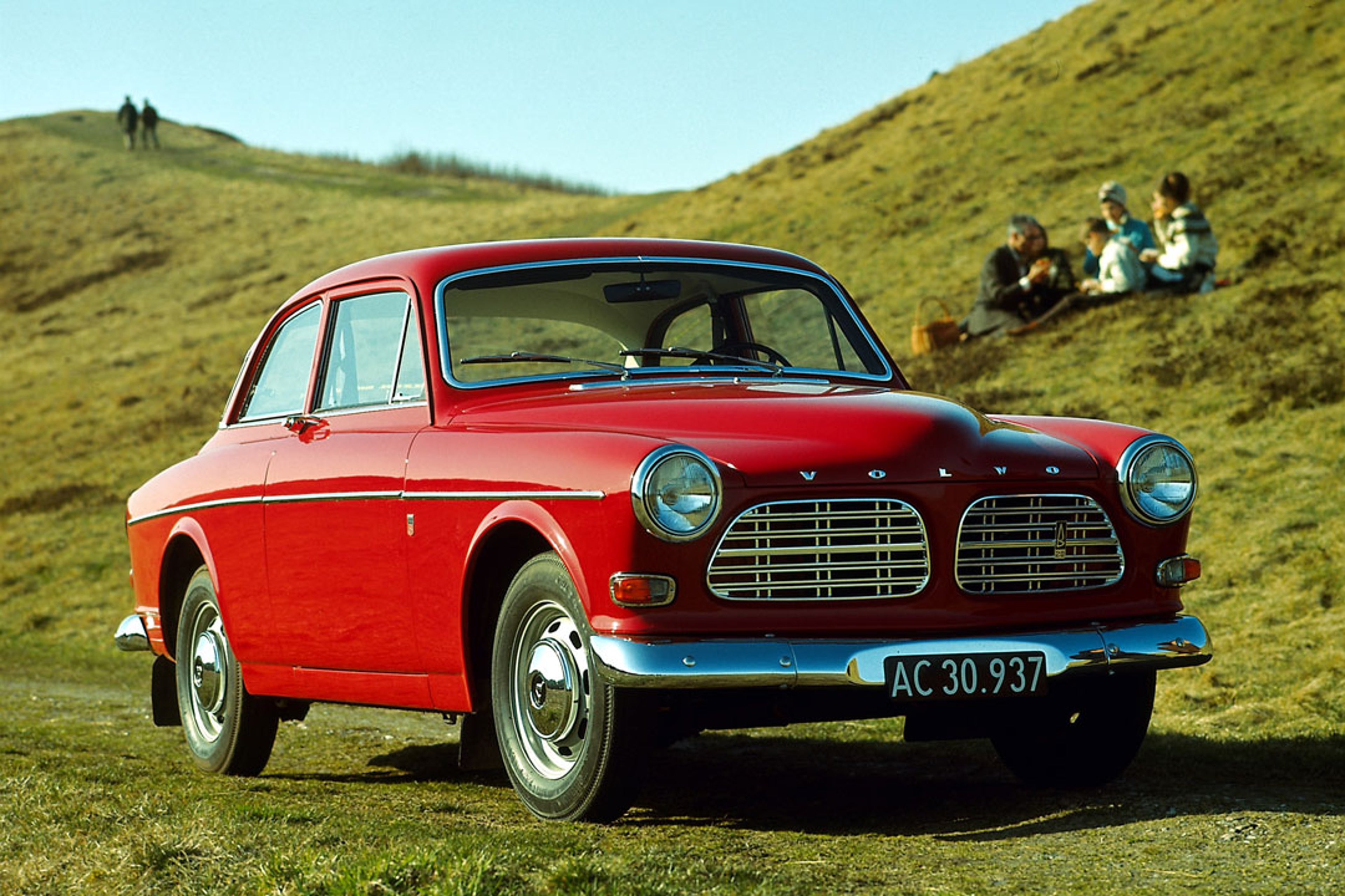 Un Volvo P130 Amazon rojo aparcado en un verde paisaje montañoso.
