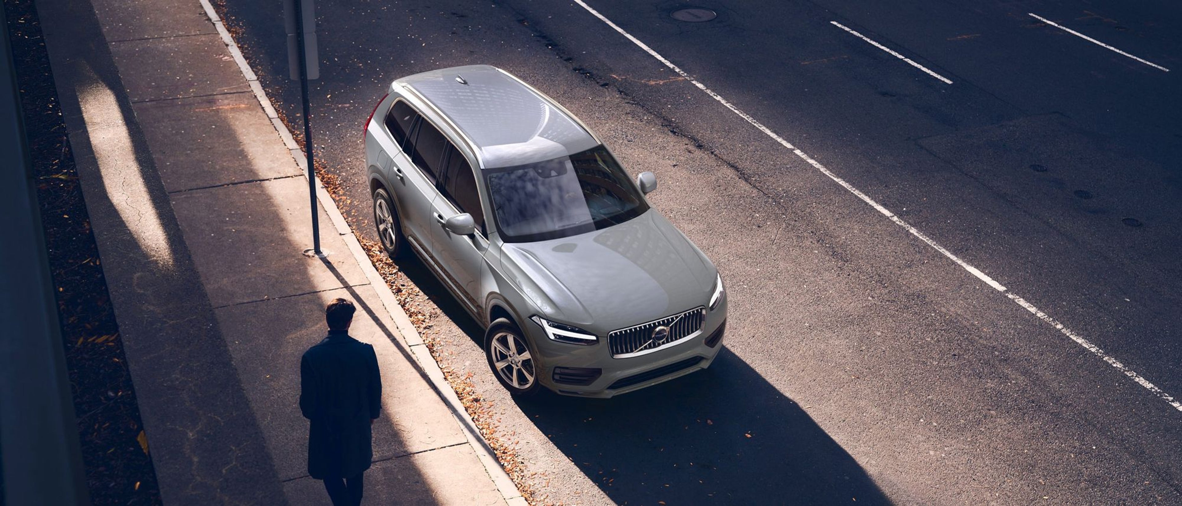 Silhouette d'une personne à côté d'une Volvo XC90 garée dans la rue.