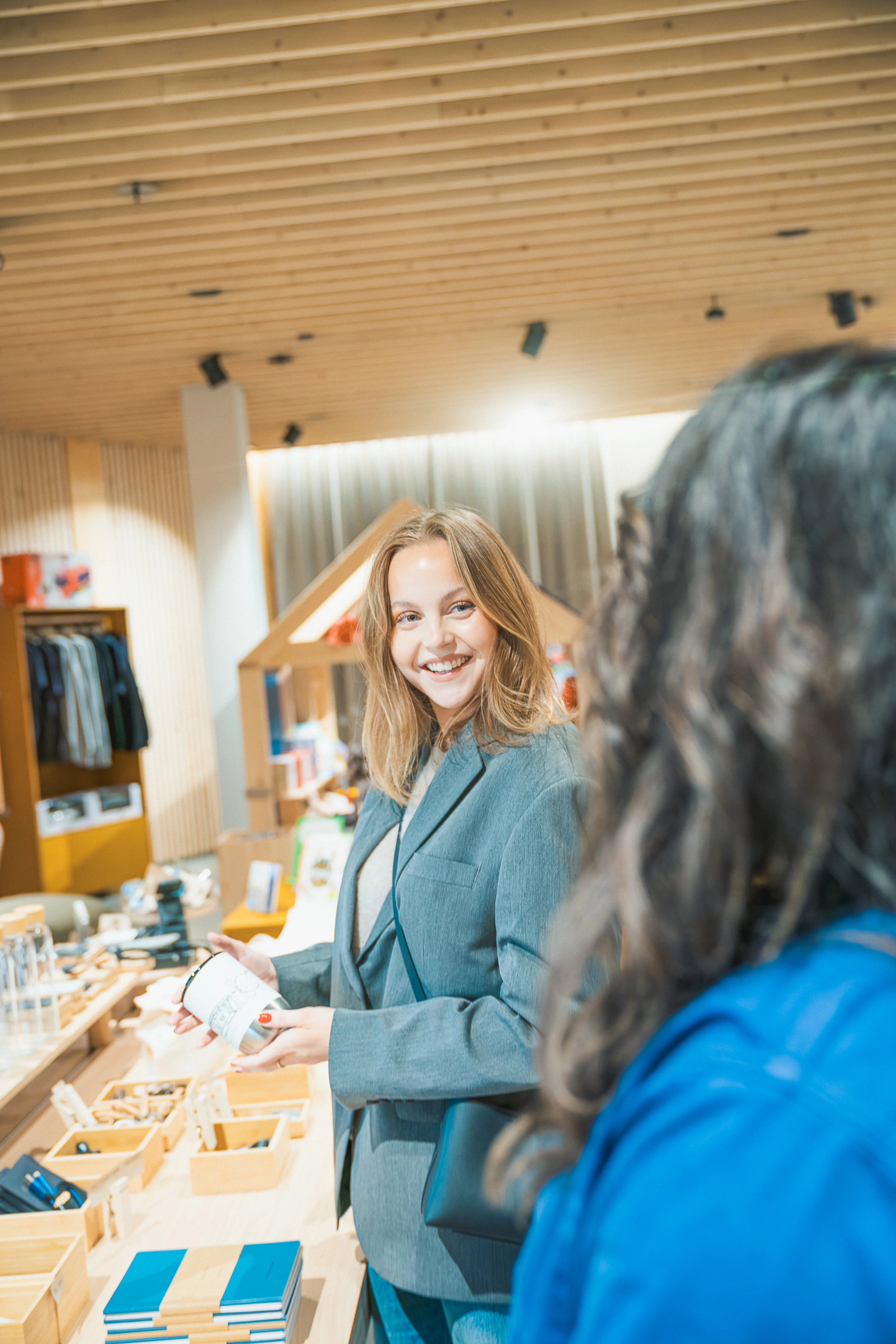 Person in blue jacket holds a green and yellow gift bag labeled "Gothenburg, Sweden" at a retail counter, with another paper bag and documents visible on the counter.