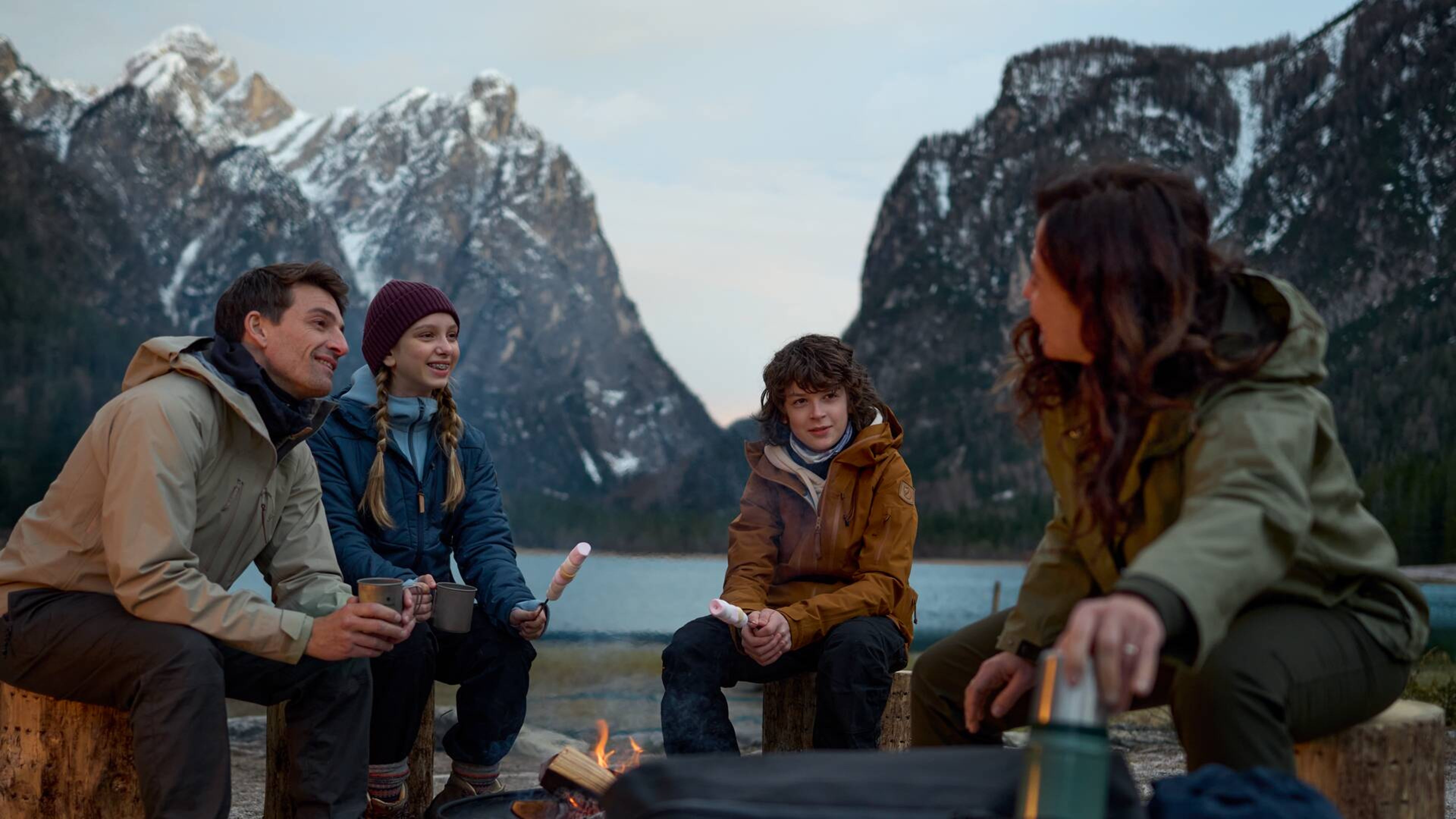 山間の湖のほとりで焚き火の前に座る家族