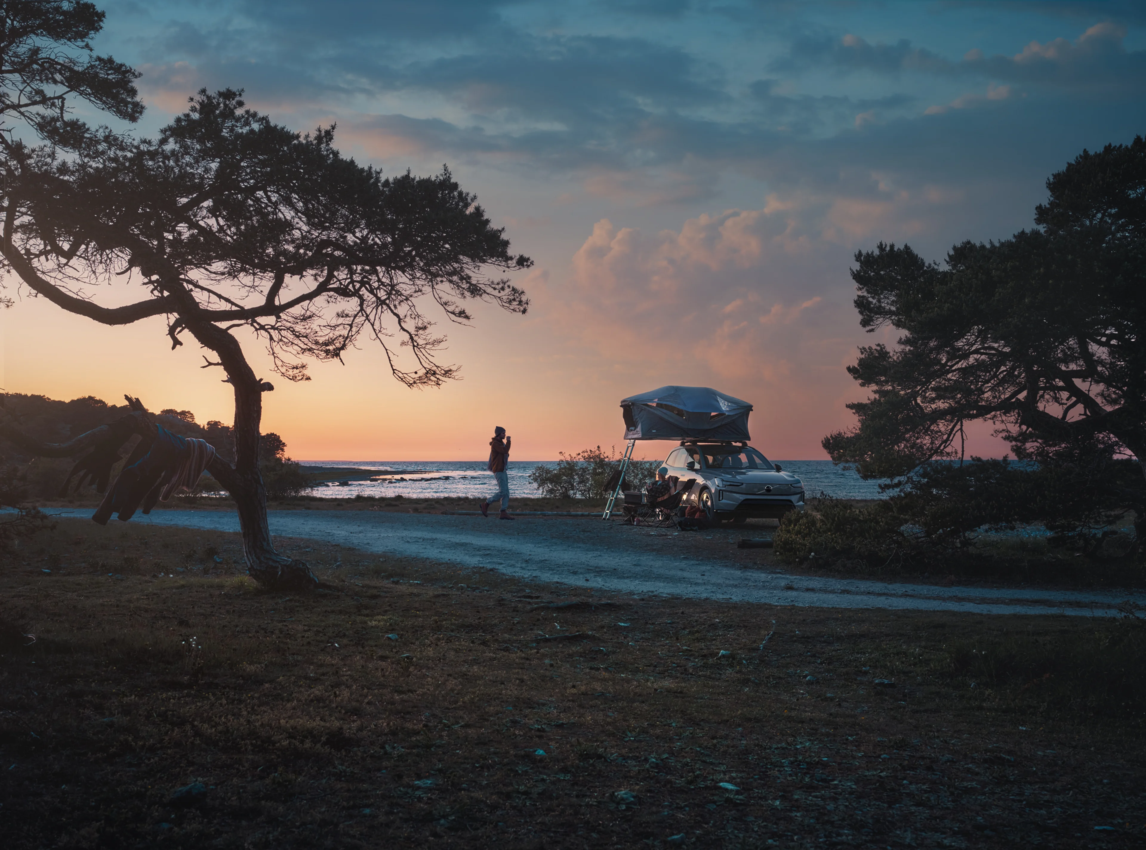 Ljudi kampiraju u prirodi s krovnim šatorom sigurno postavljenim na krov svog parkiranog Volva.