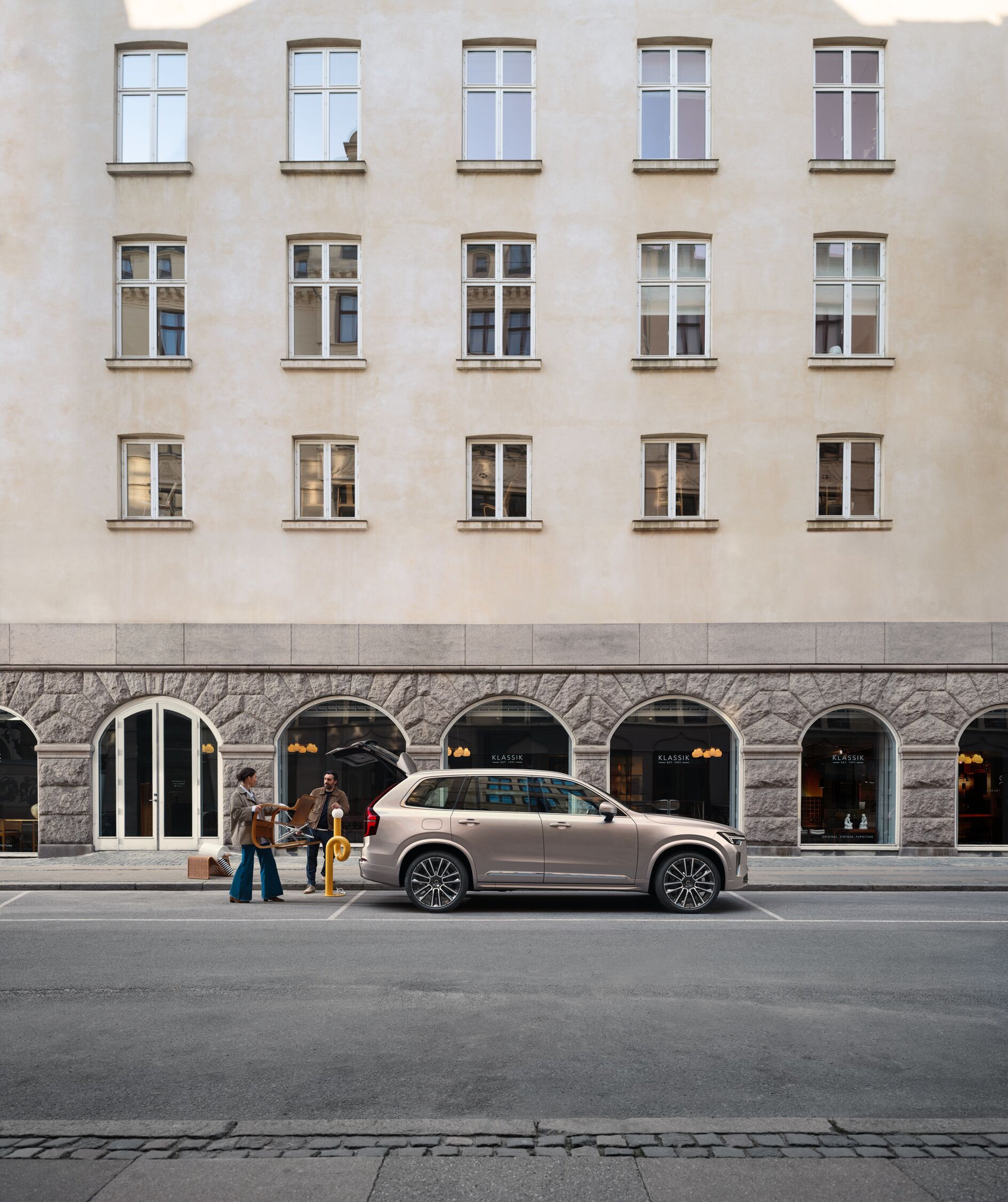 Modern, stylish restaurant interior with curved wooden ceiling, ambient lighting, and people dining. Large windows reveal a Volvo XC40 parked inside, visible near the back of the space.
