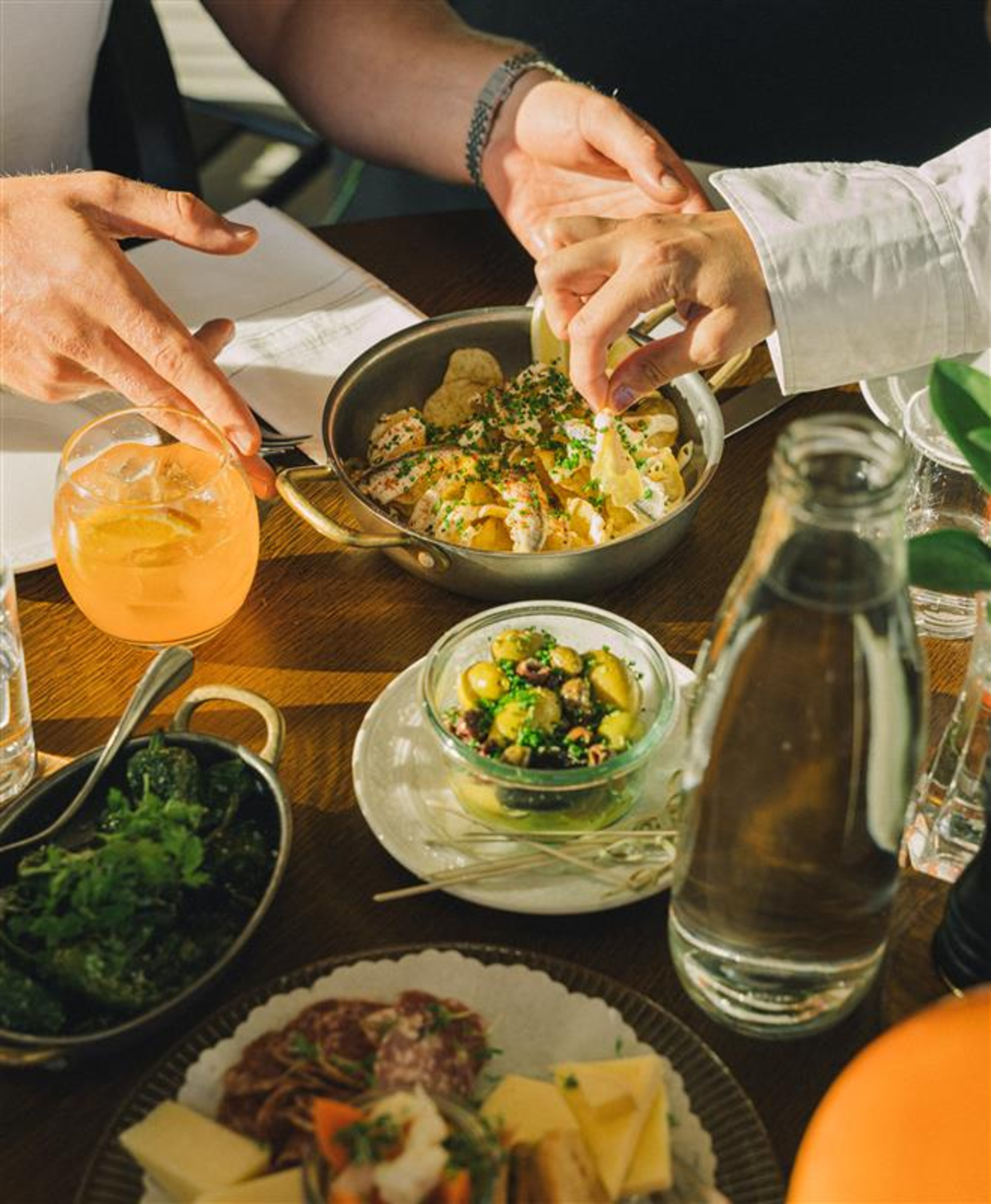 A close-up of a gourmet salad topped with shredded cheese and fresh herbs, served on a clear glass plate on a wooden table set for a meal.