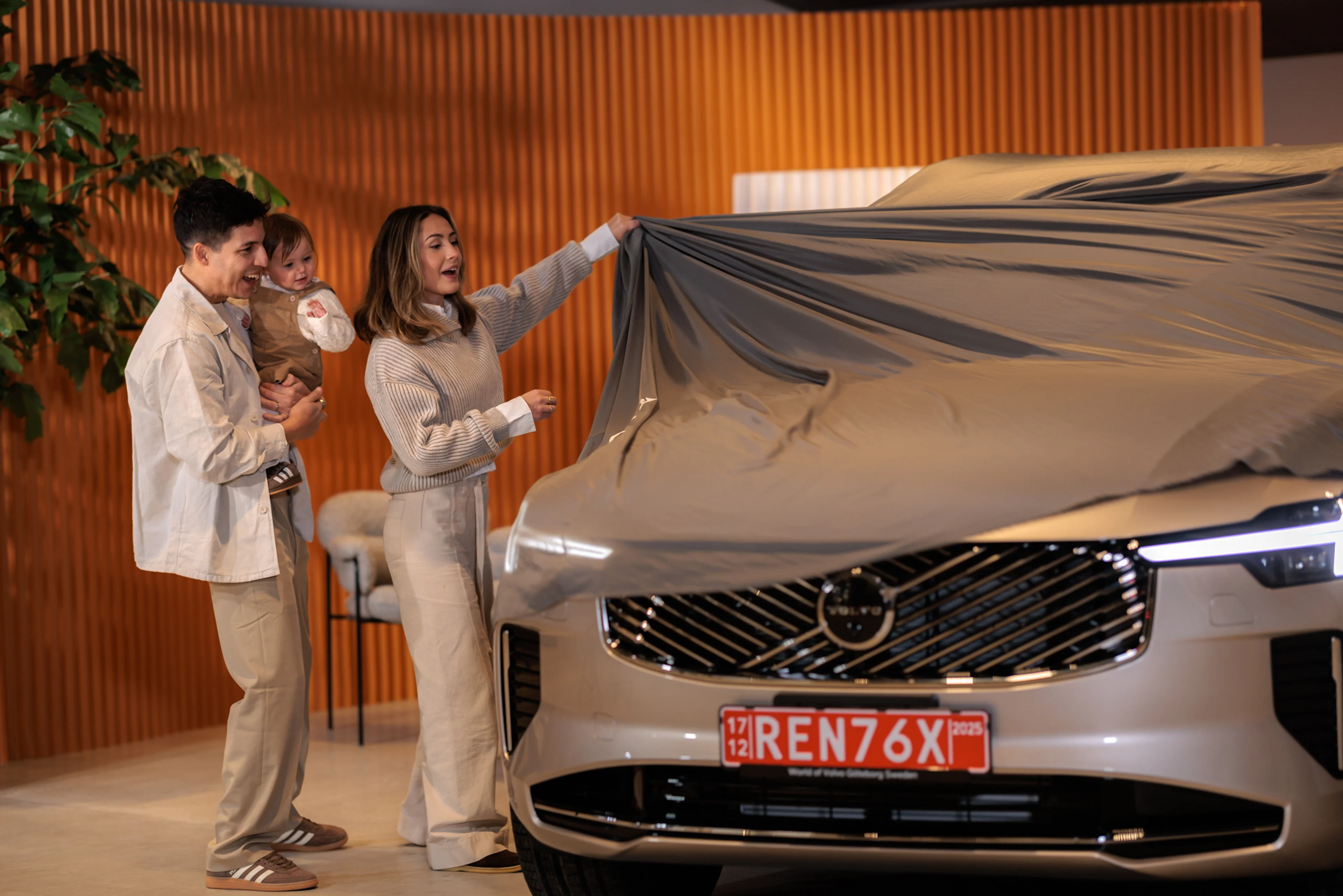 A light blue Volvo EX30 electric SUV drives along a city street lined with modern and historic buildings, showcasing its sleek design and compact urban-friendly size.
