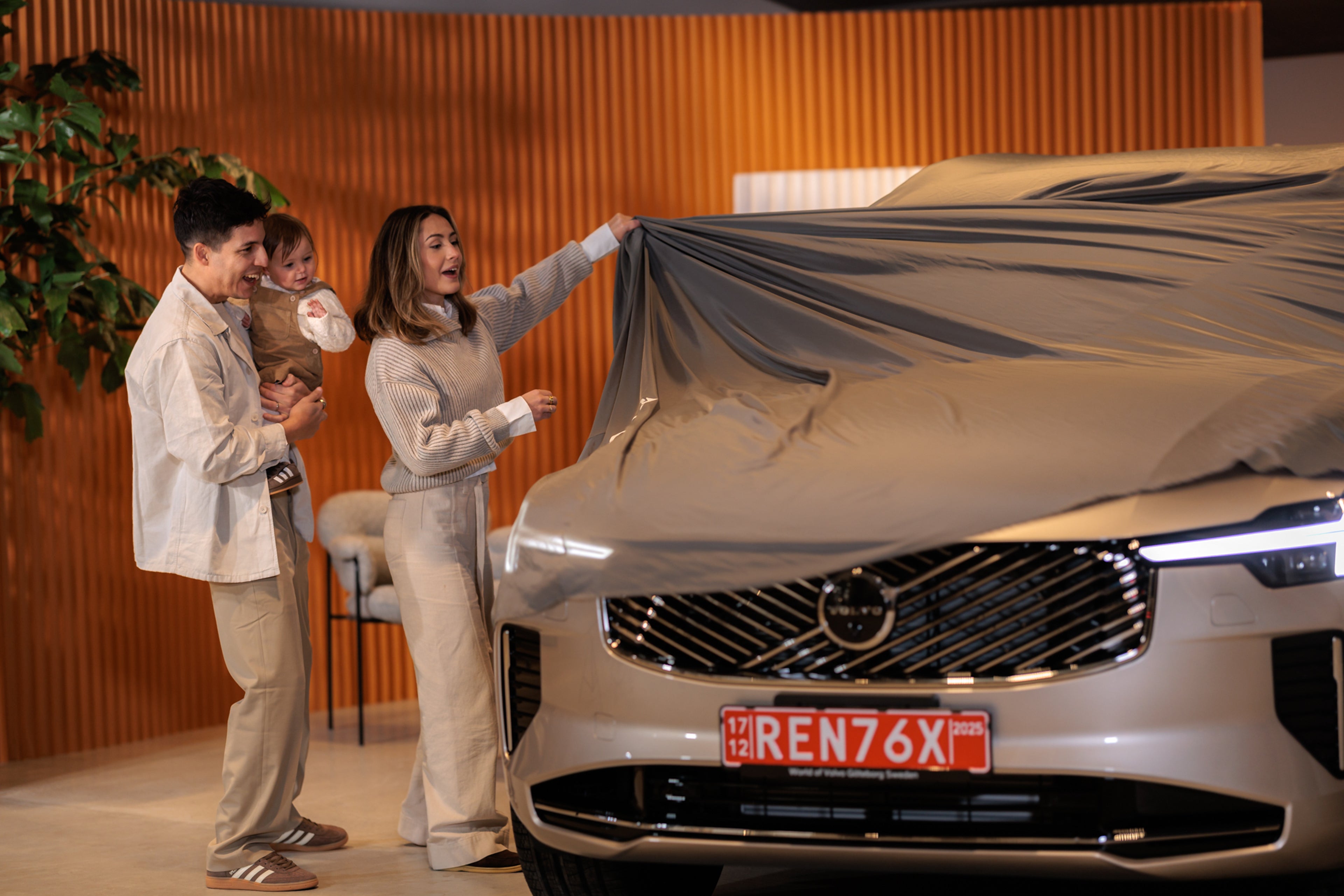 A light blue Volvo EX30 electric SUV drives along a city street lined with modern and historic buildings, showcasing its sleek design and compact urban-friendly size.