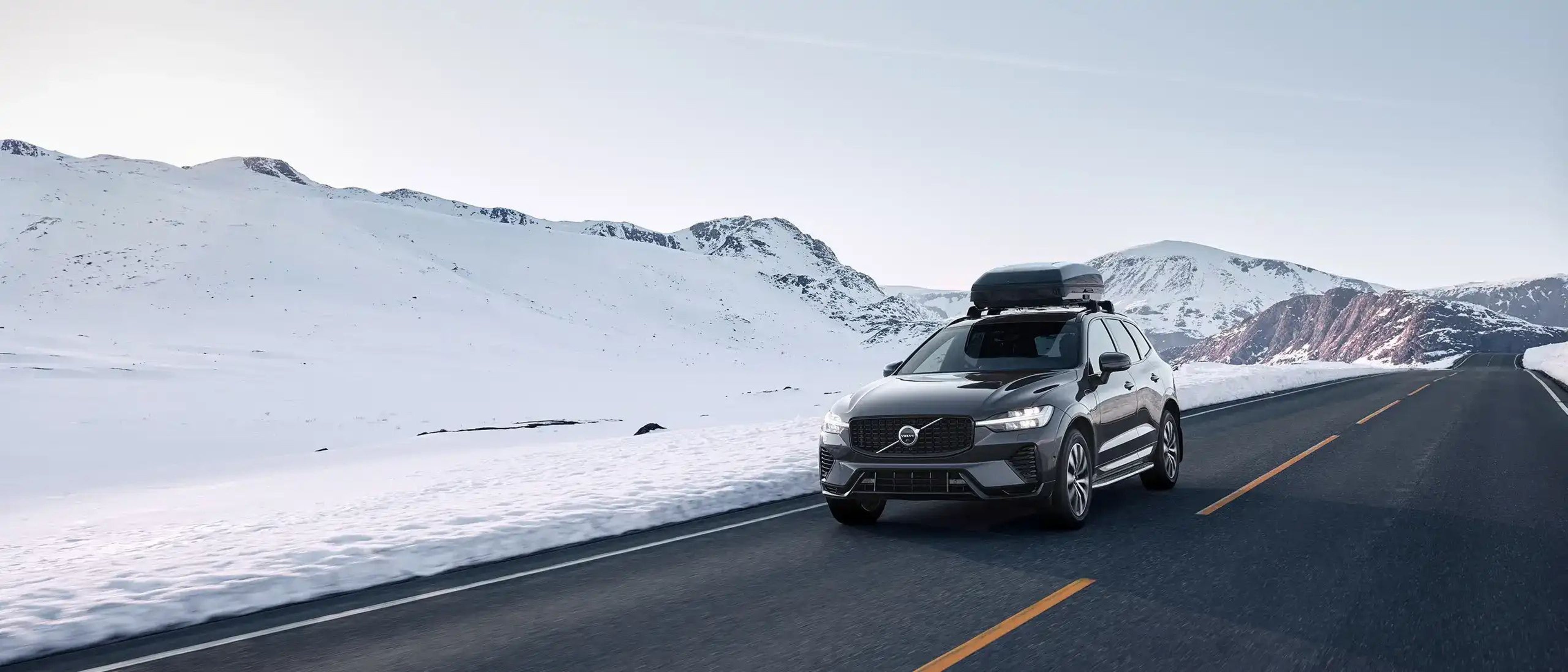 Egy tetőboxszal felszerelt Volvo XC60 havas terepen halad.