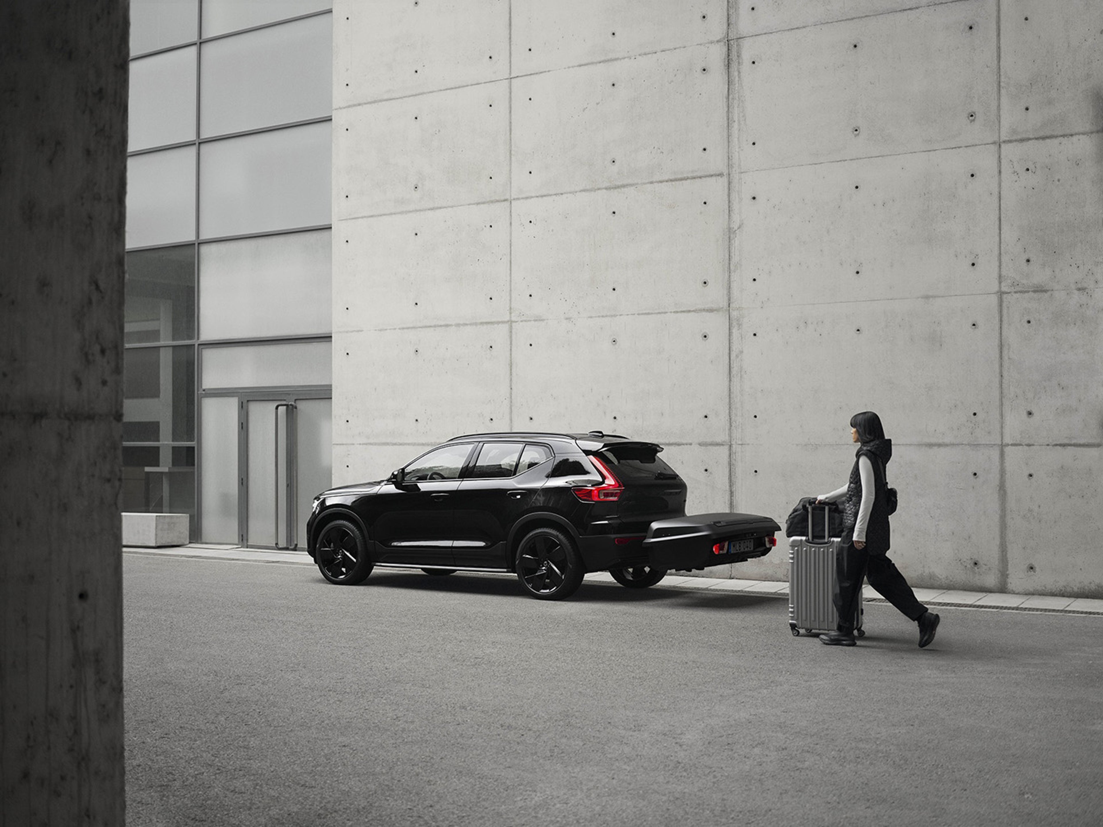 Egy nő bőrönddel a Volvo vonóhorogra szerelhető csomagszállító doboza felé sétál.