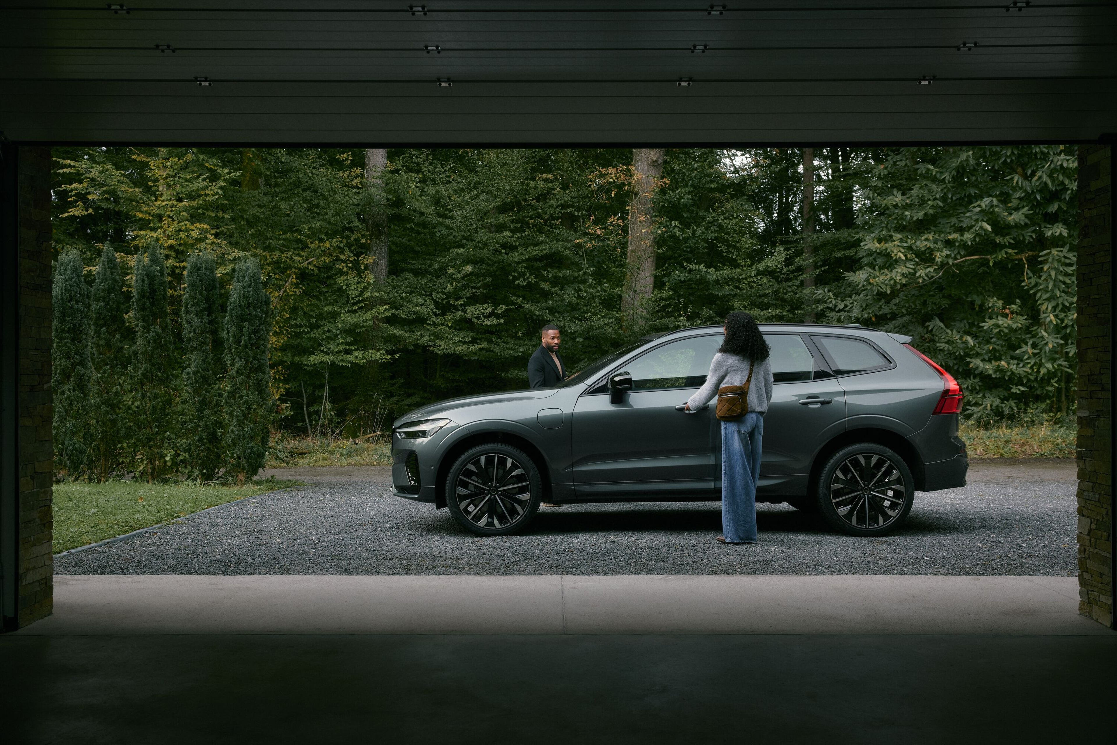 A white Volvo XC60 drives along a narrow, winding road surrounded by calm water on both sides, viewed from above in a serene, minimalist landscape.