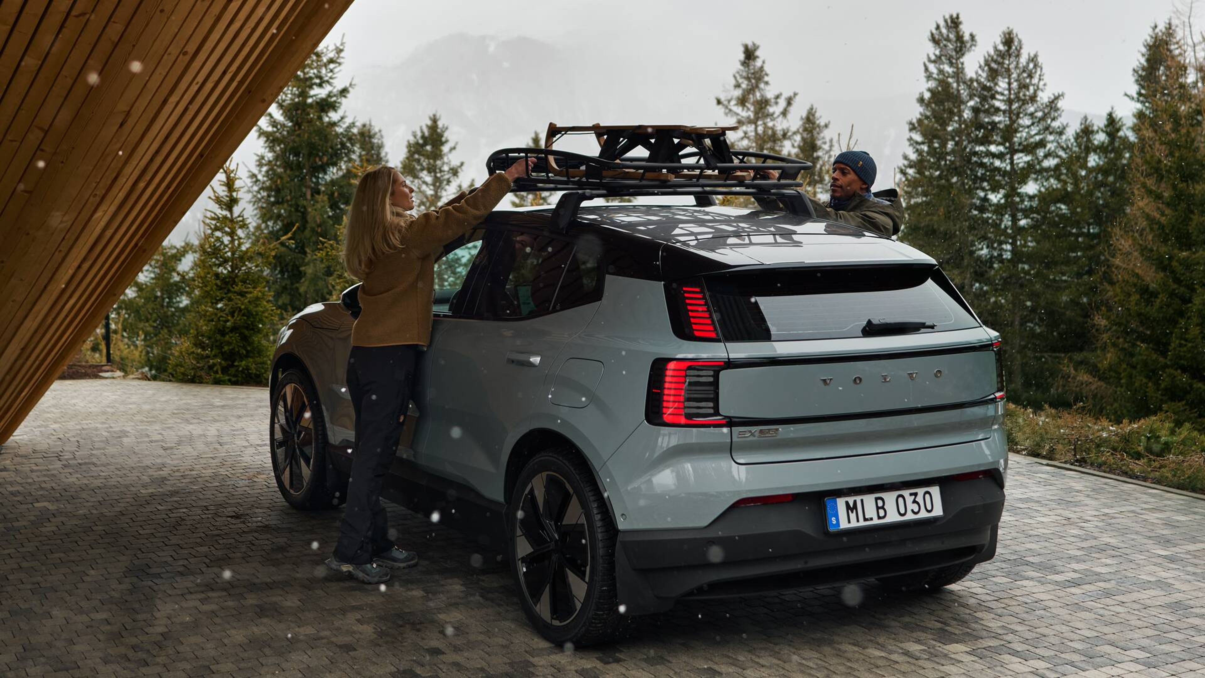 冬の風景の中、EX30のルーフバスケット(エクステンダー付き)にソリを積み込むカップル