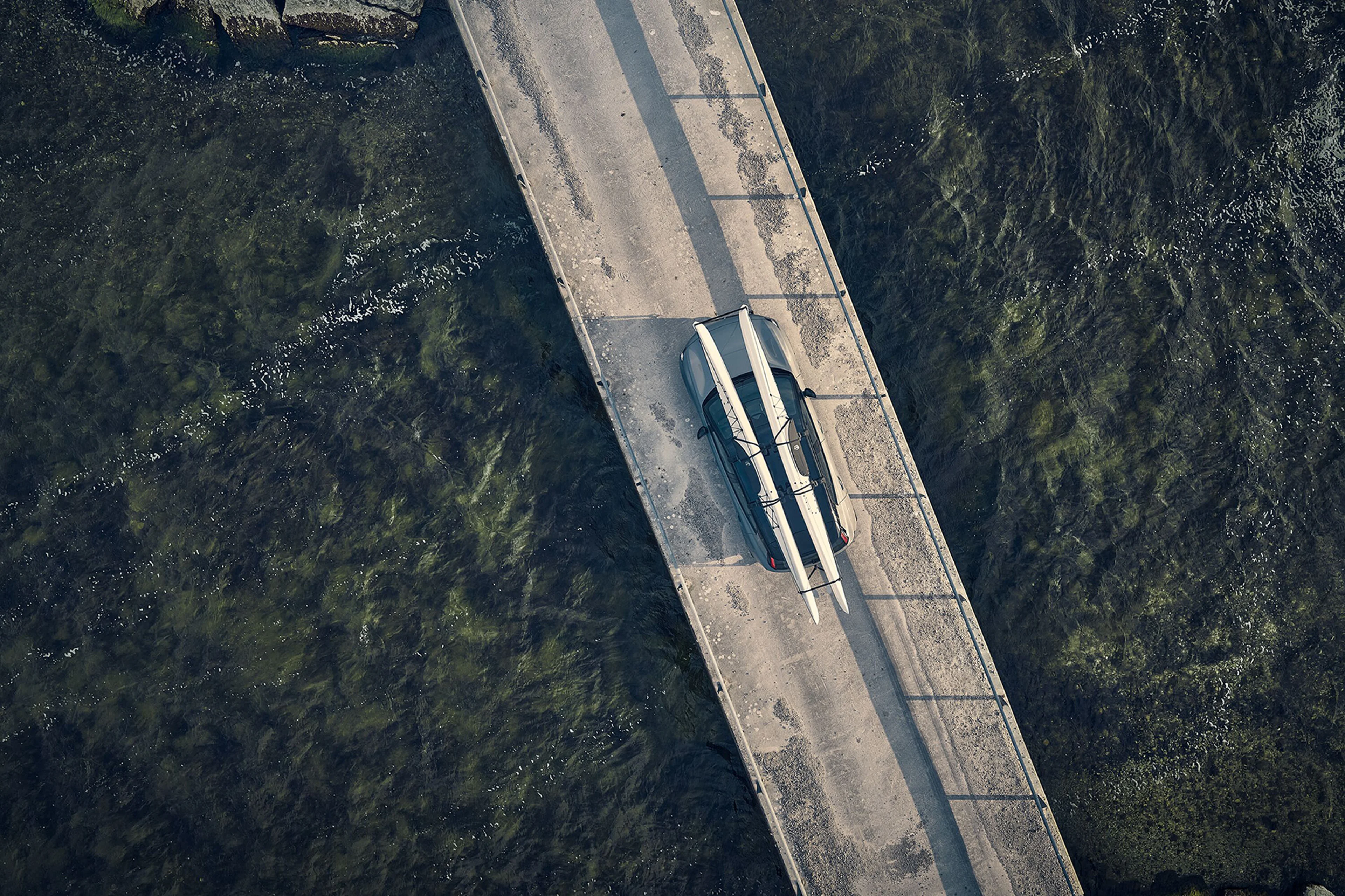 Bird’s-eye view of a Volvo car parked on a bridge over water with two kayaks mounted to the roof.