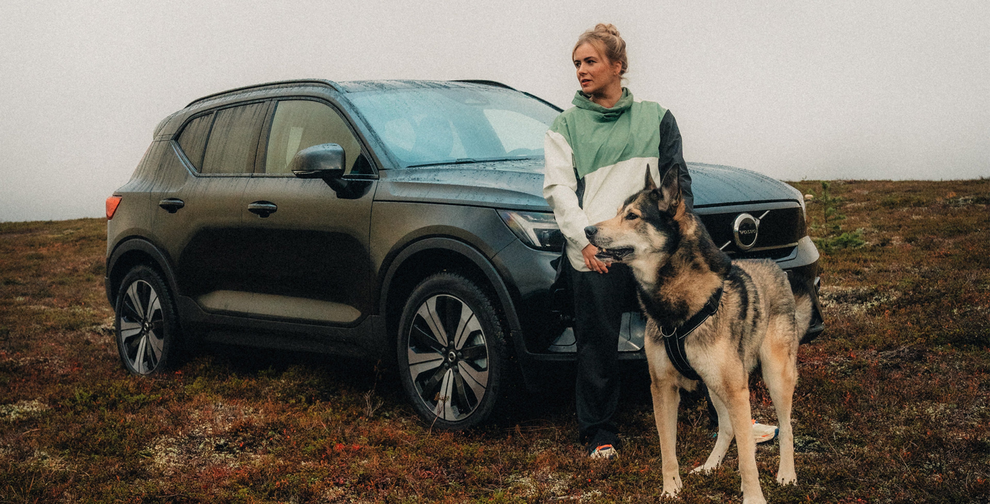 Laulaja Yona ja itäsiperianlaika Vanja Volvo XC40 täyssähköauton kanssa luontomaisemassa.
