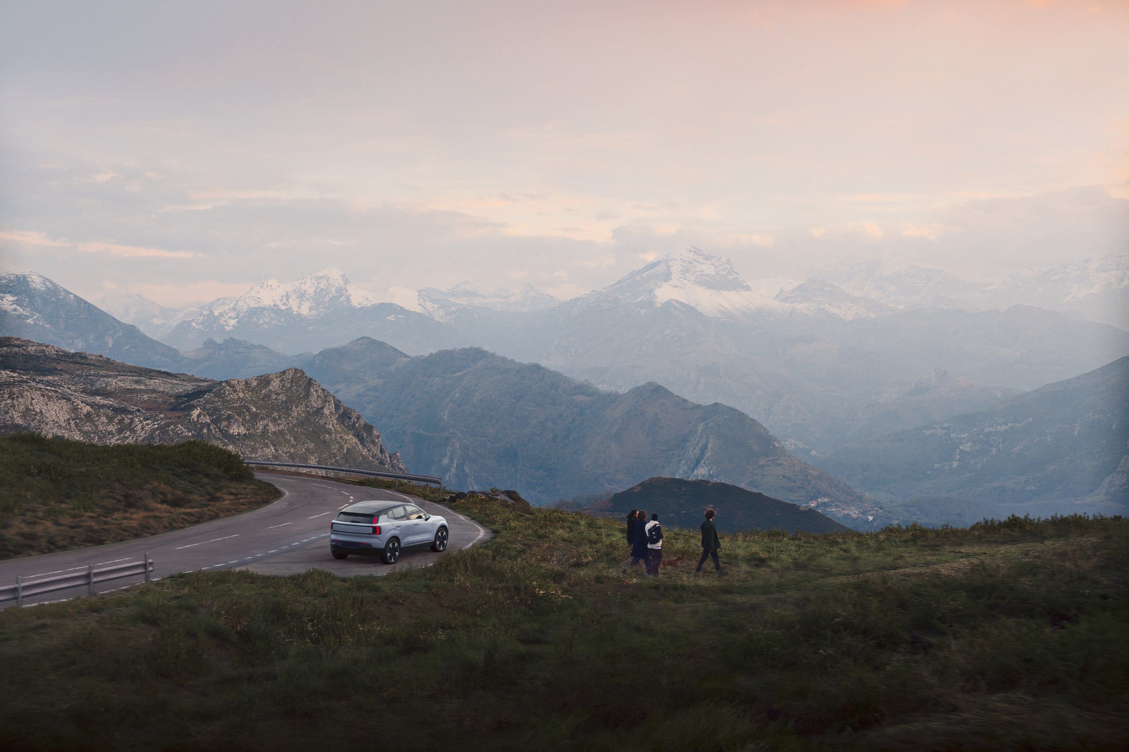 Ein Volvo EX30 steht auf einer Landstraße in einem gewaltigen Bergpanorama. Die drei Insassen steigen aus, um sich die Landschaft anzusehen.