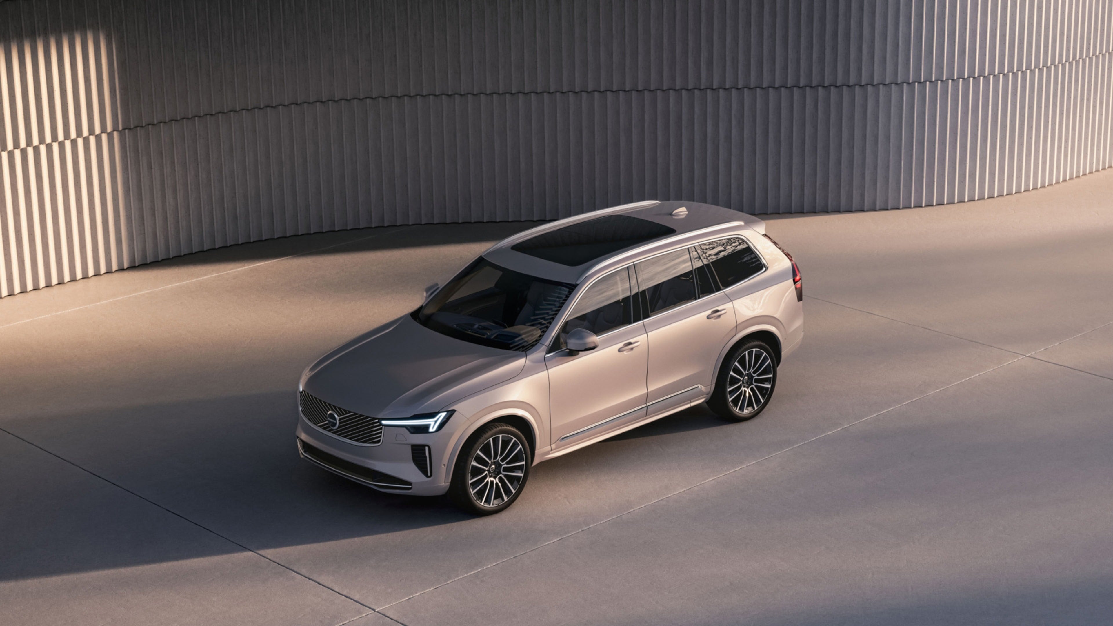 SUV XC90 argenté garé près de la côte au coucher du soleil, avec un ciel et un océan en arrière-plan.)