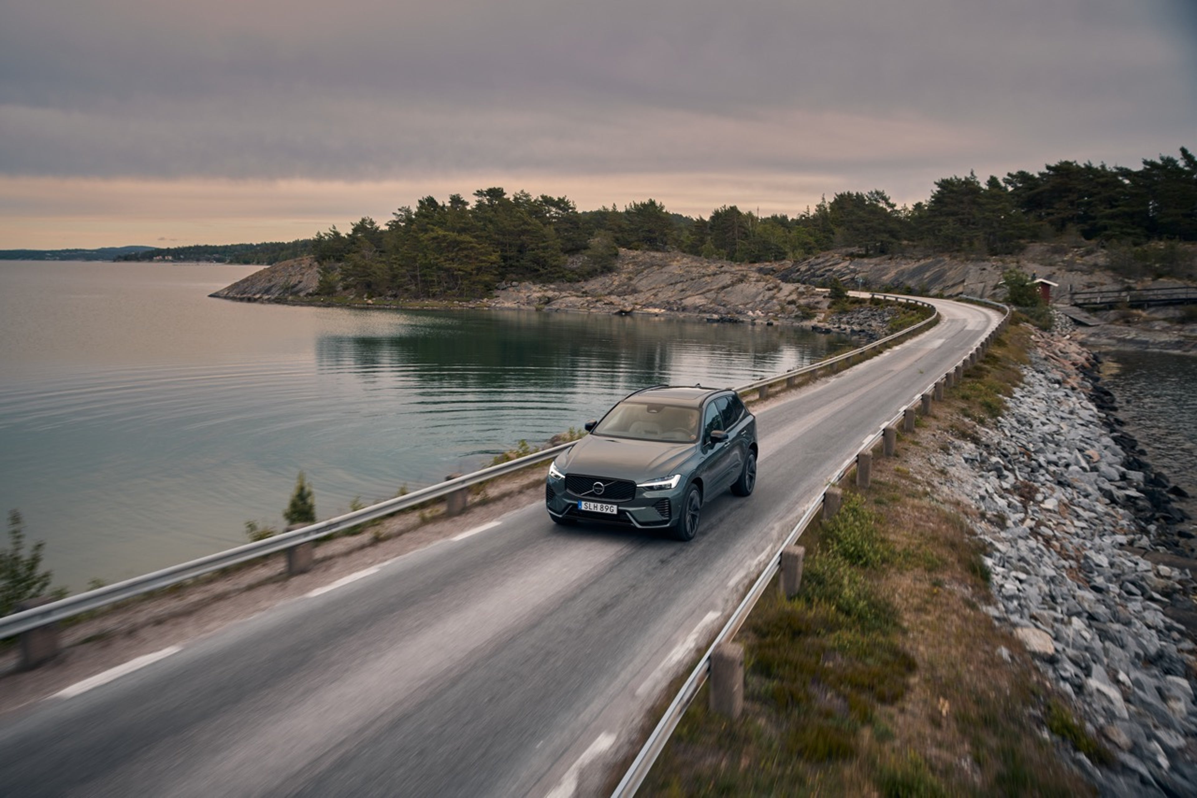 A grey Volvo XC60 driving on a road beside the Swedish coastline at sunset.